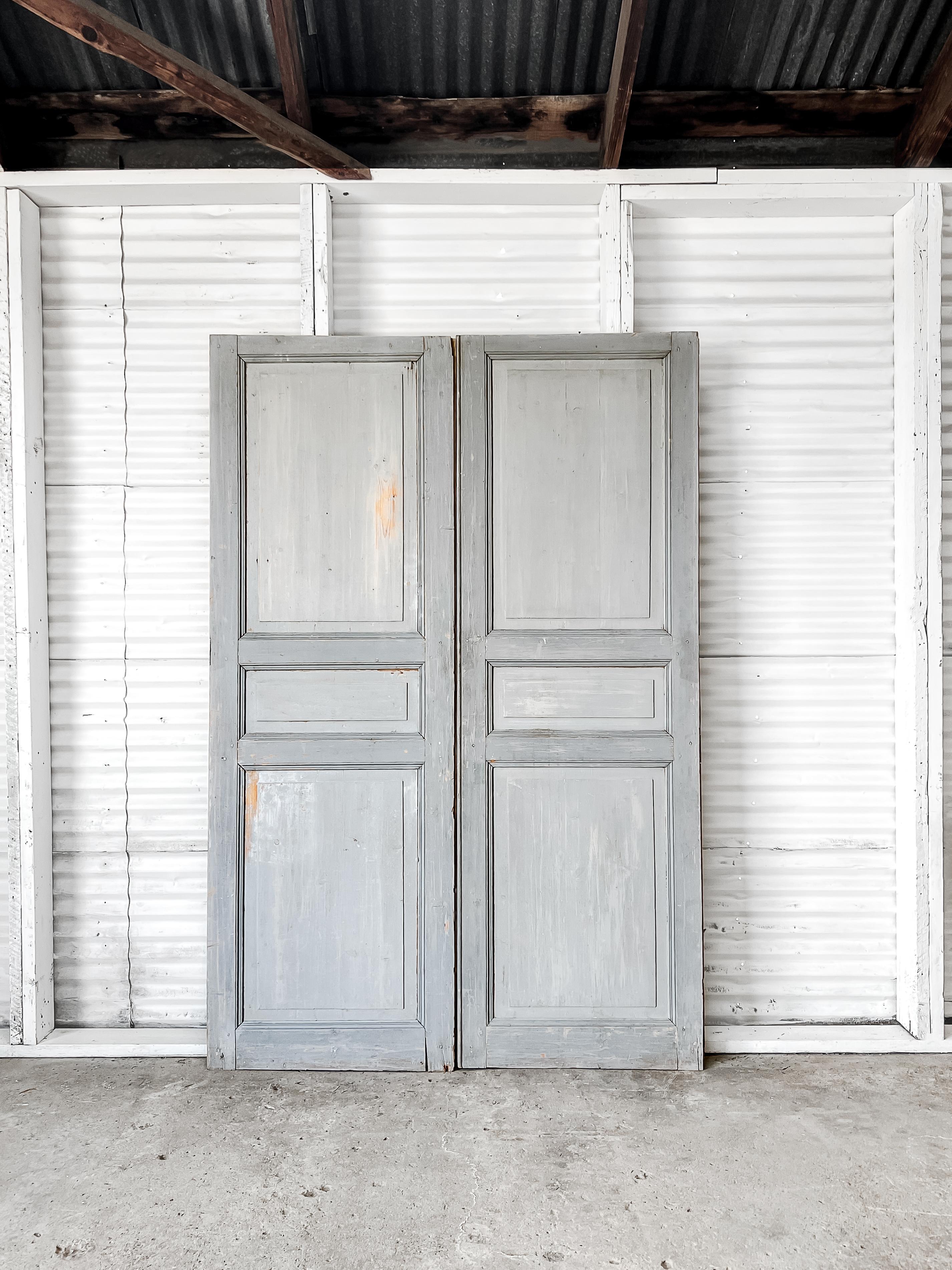 A pair of 19th-century antique French wardrobe doors. Handcrafted from solid wood, the doors feature three panels with grooved beveled trim painted in a two-tone color scheme of pale shades of blue.

The doors would be best installed to enclose a