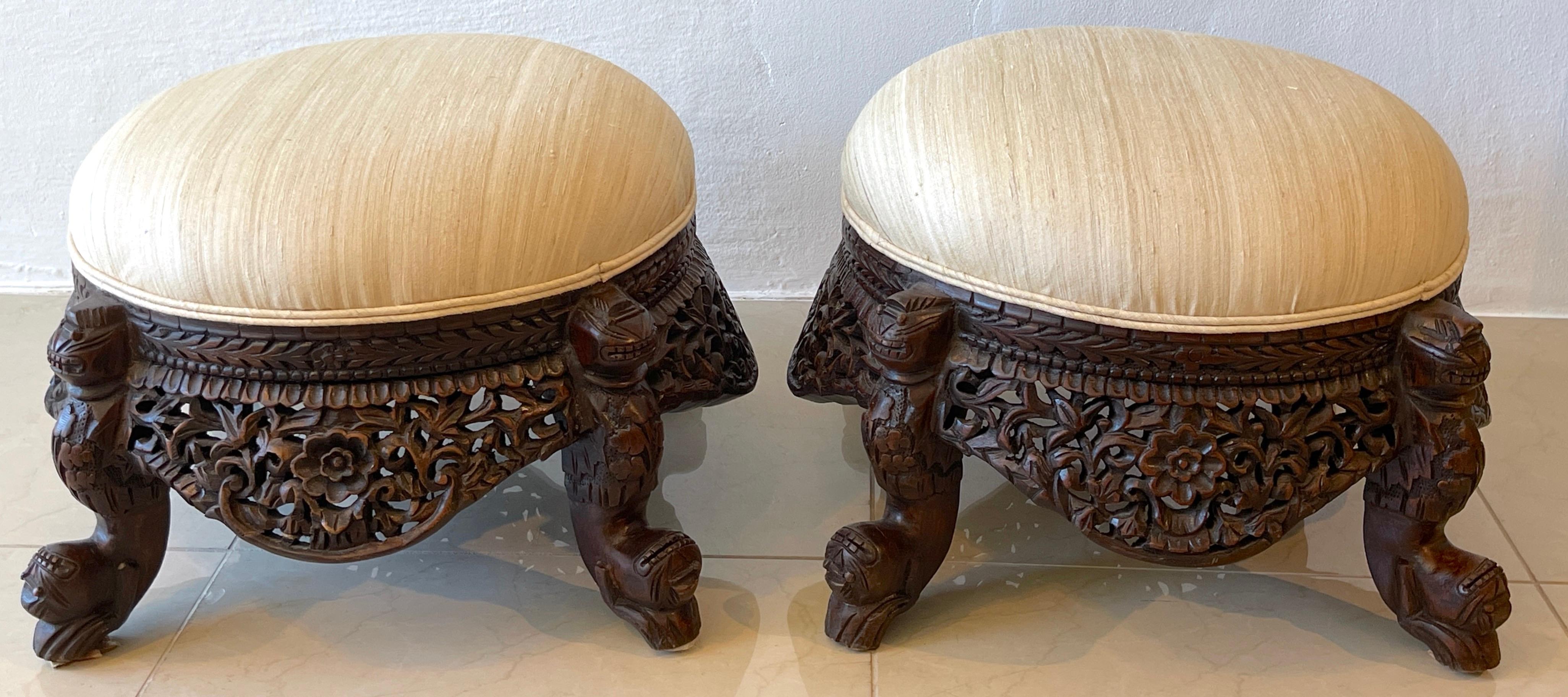 Pair of 19th century Anglo-Indian carved footstools 
Each one with exceptional pierced figural carving, with newly upholstered cushions in a subtle neutral stripped silk. Raised on four figural caryatid splay legs.
The diameter of the top cushion