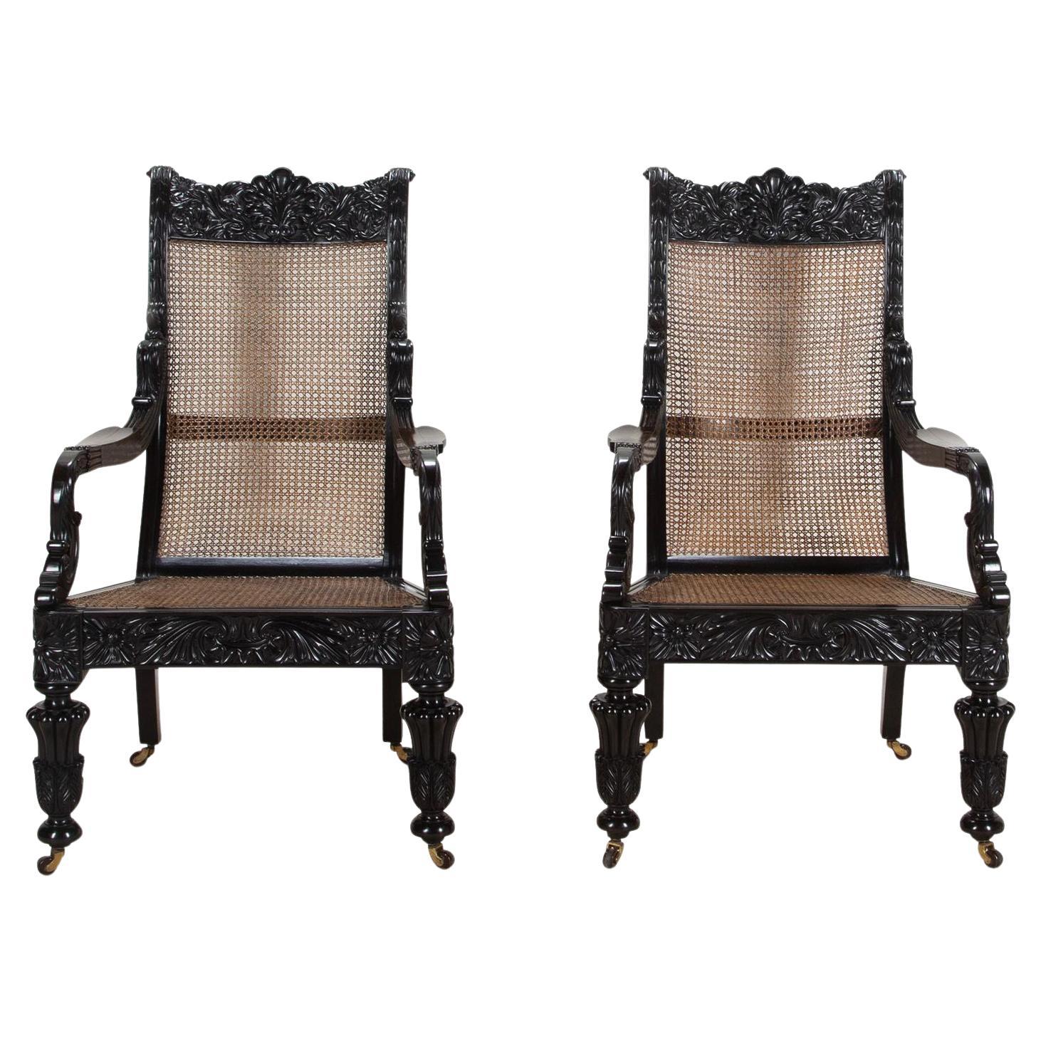A splendid pair of 19th Century Anglo-Indian carved ebony open arm library chairs; finely carved in solid ebony. 

From the Galle District, Ceylon (Sri Lanka). The shaped crest rails finely carved with a large central scallop shell flanked by