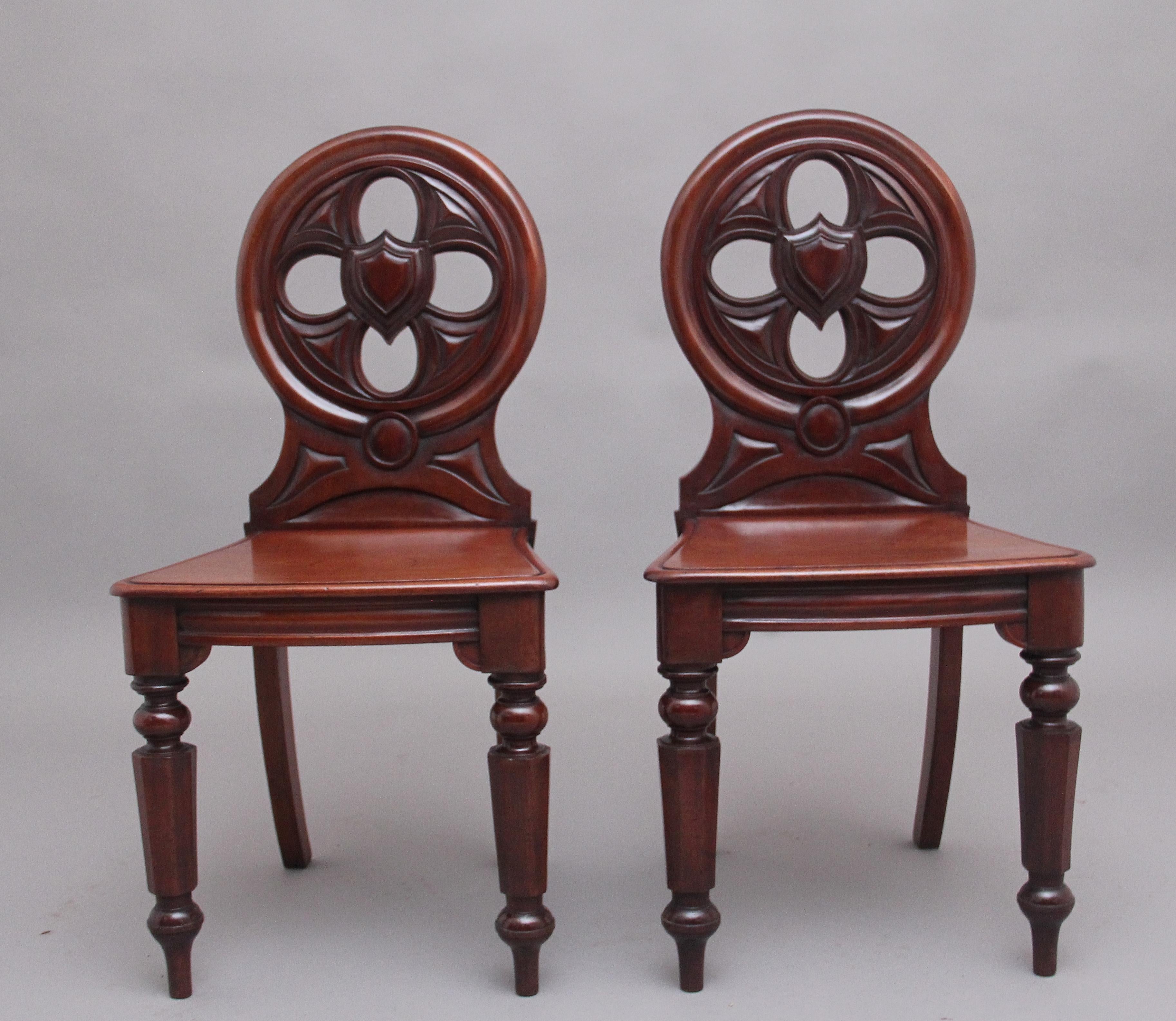 A pair of mid 19th Century mahogany hall chairs, having circular shaped and moulded backs and centred by shield reserves, hard seats with nice figuration, supported on out swept rear legs and turned front legs. Circa 1840.
  