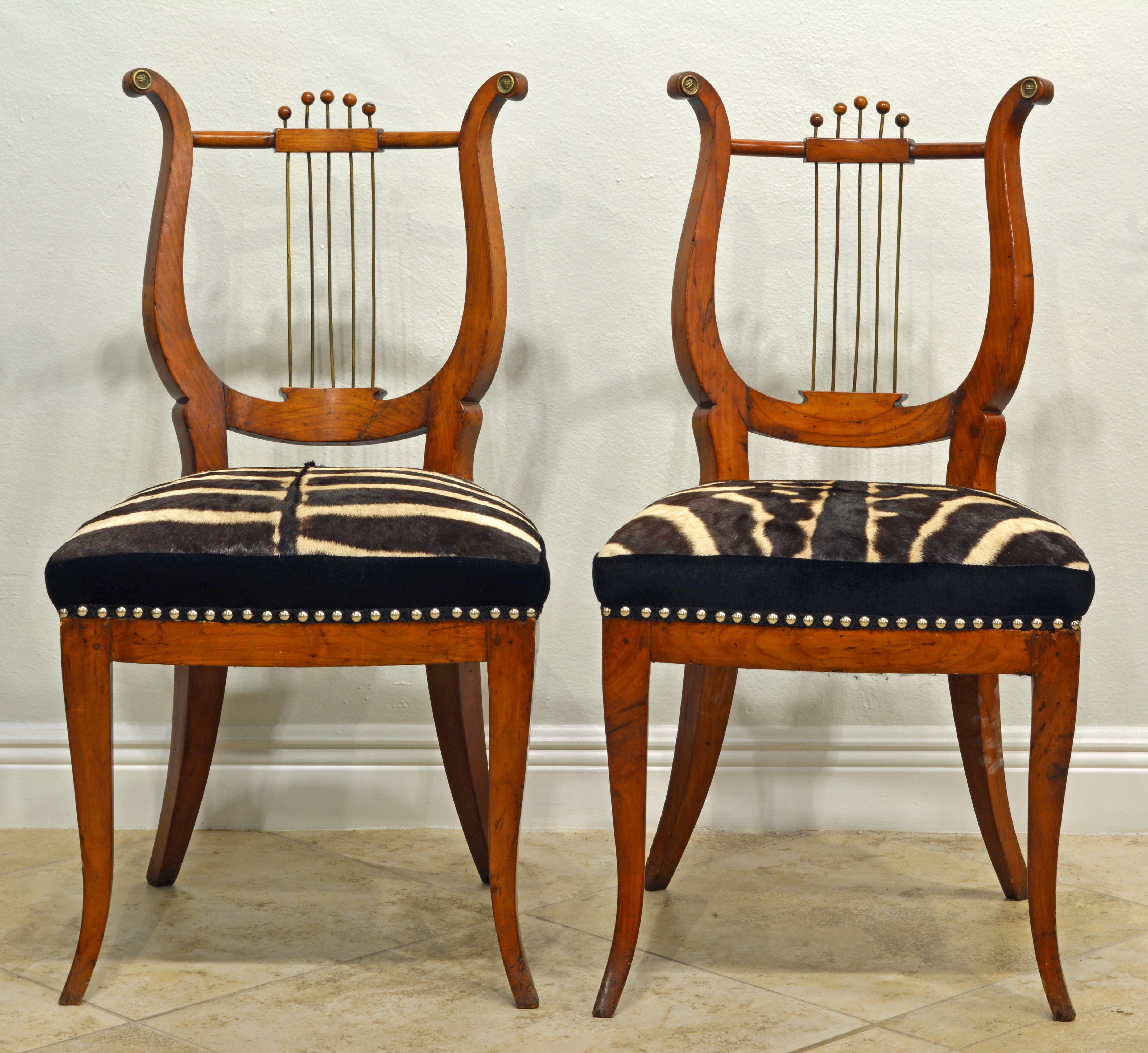This lovely and unusual pair of Austrian neoclassical musical themed chairs date to the early 1800s and could also be characterized as early Biedermeier style. The backs are very elegant with a combination of a shaped fruit-wood frame incorporating