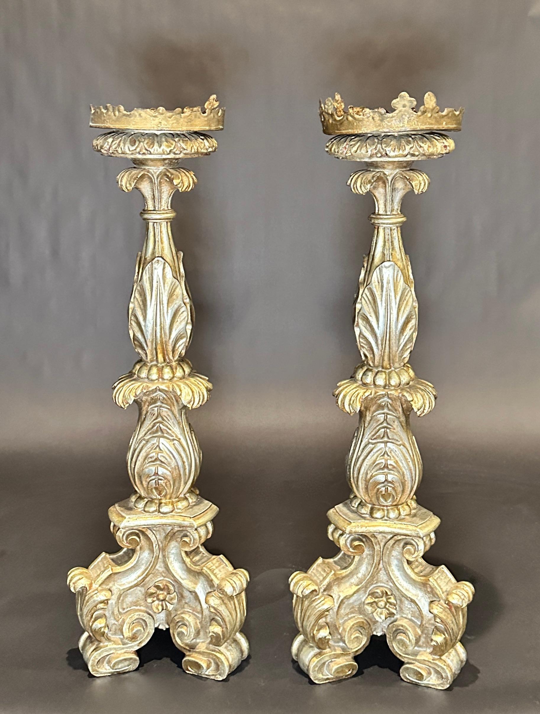 Superbe paire de chandeliers en bois doré sculpté à la main, de style baroque italien du XIXe siècle, à base tripode et à pied. Ces magnifiques chandeliers sont de grande taille, dorés à l'argent et ornés de sculptures. Bois doré à l'argent avec