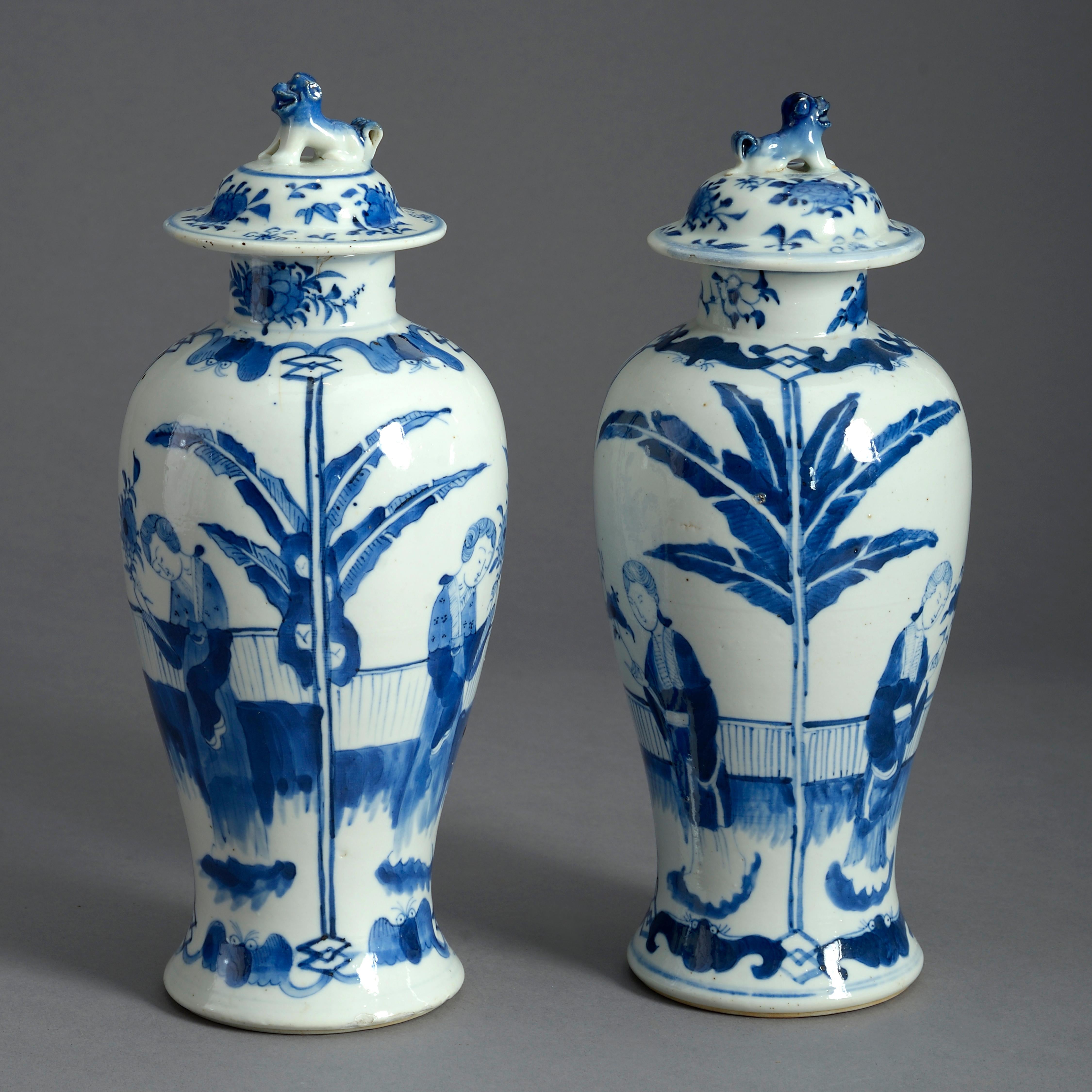 A pair of mid-nineteenth century blue and white glazed porcelain vases of baluster form, the lids surmounted by stylised lions, the bodies decorated with palm trees and court figures. Each with four character marks to the underside.

Qing