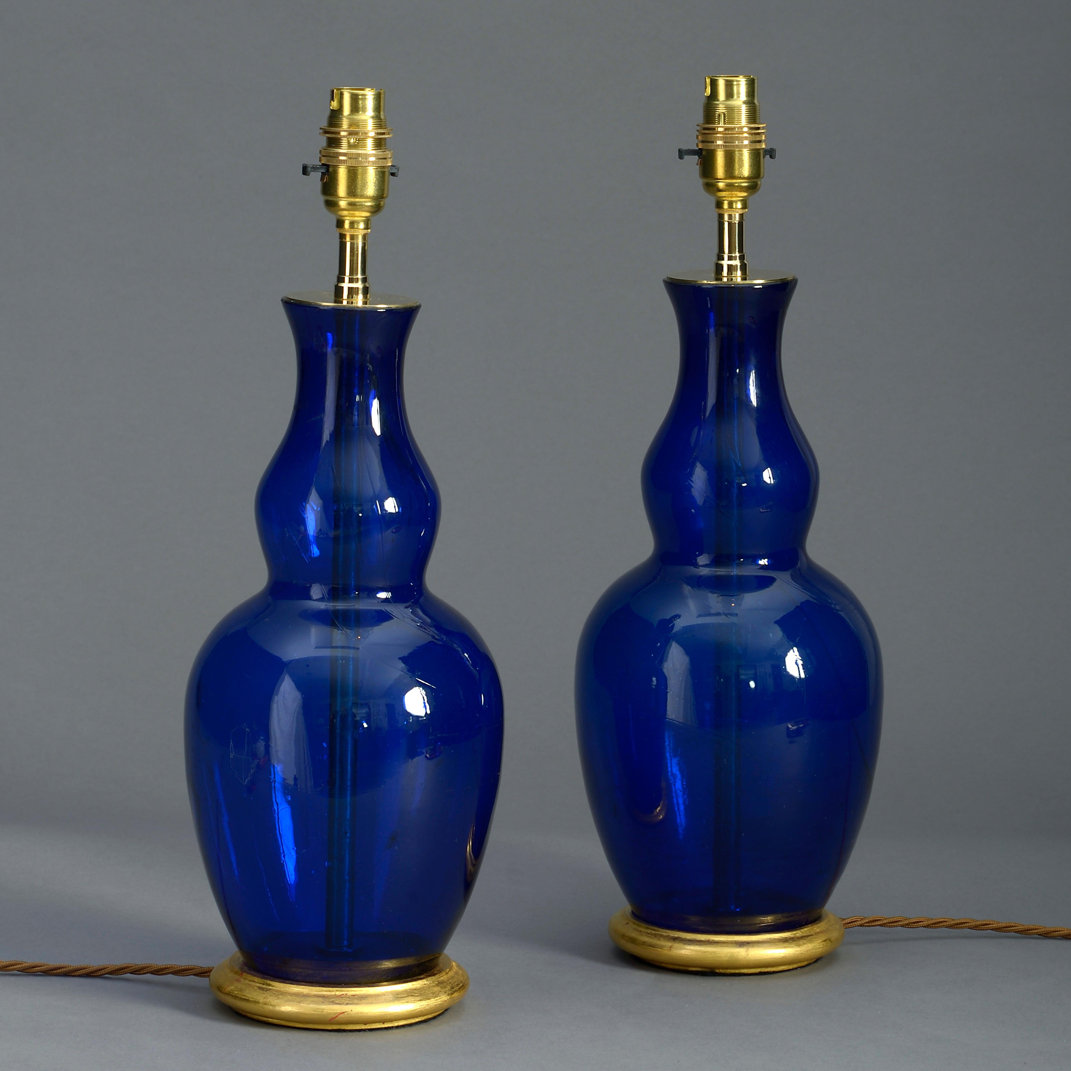 A pair of late nineteenth century Bristol blue glass gourd vases of deep color. Now mounted on turned giltwood bases and wired as electric table lamps.

Dimensions refer to glass and giltwood elements.

     