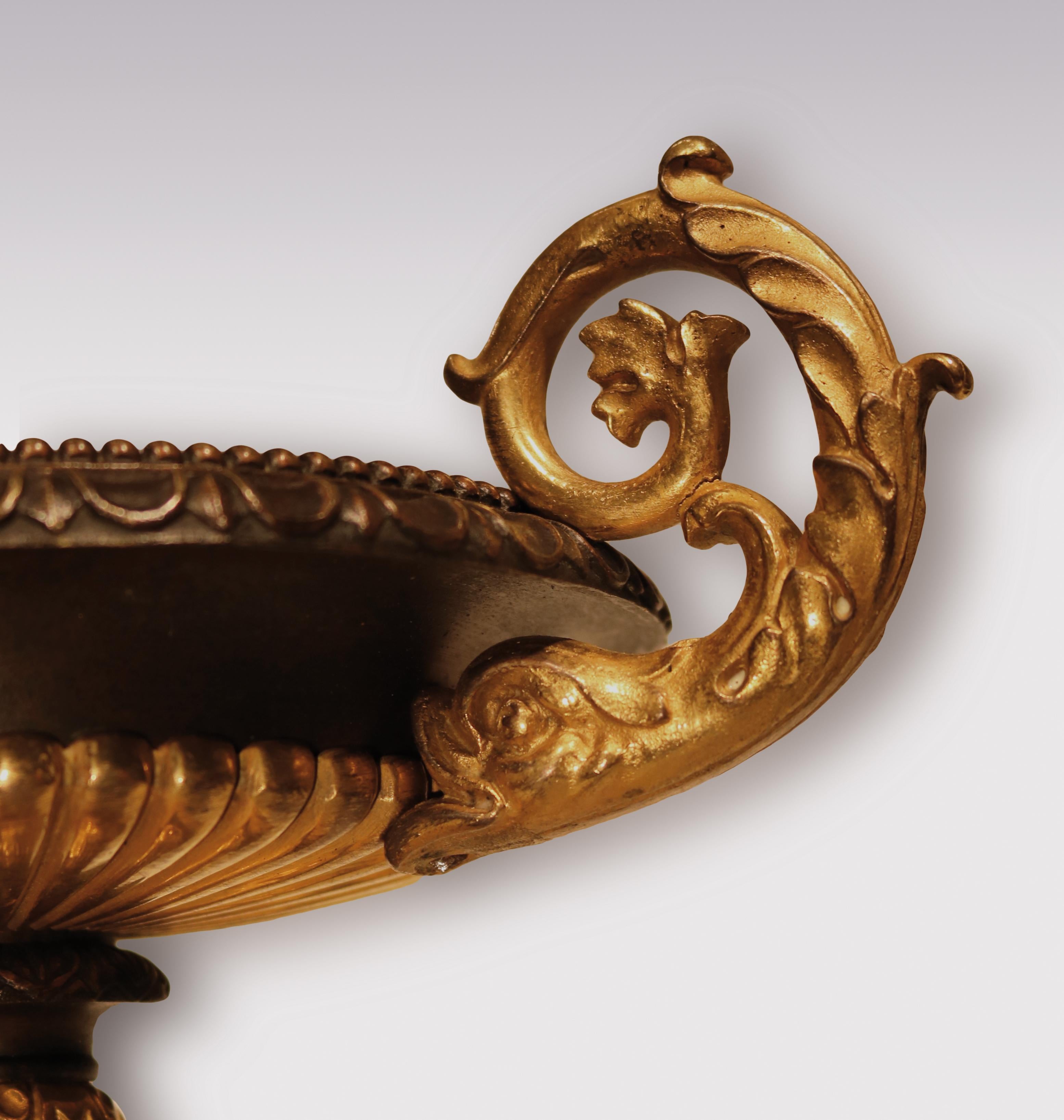 A pair of early 19th century bronze and ormolu tazzas having beaded and leaf decorated rims and unusual dolphin carrying handles, supported on Sienna marble bases.