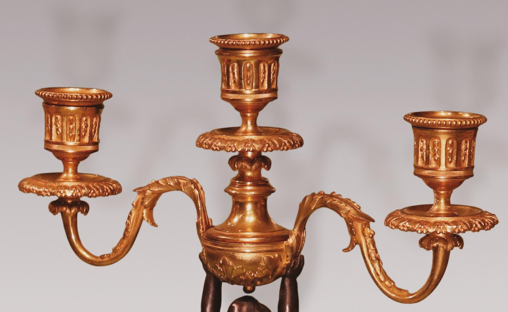A pair of mid-19th century bronze and ormolu three-light candelabra, in the form of well-cast cherubs holding urns with well scrolled candle-arms, raised on wreath & beaded decorated socles, ending on white marble plinths on turned feet.