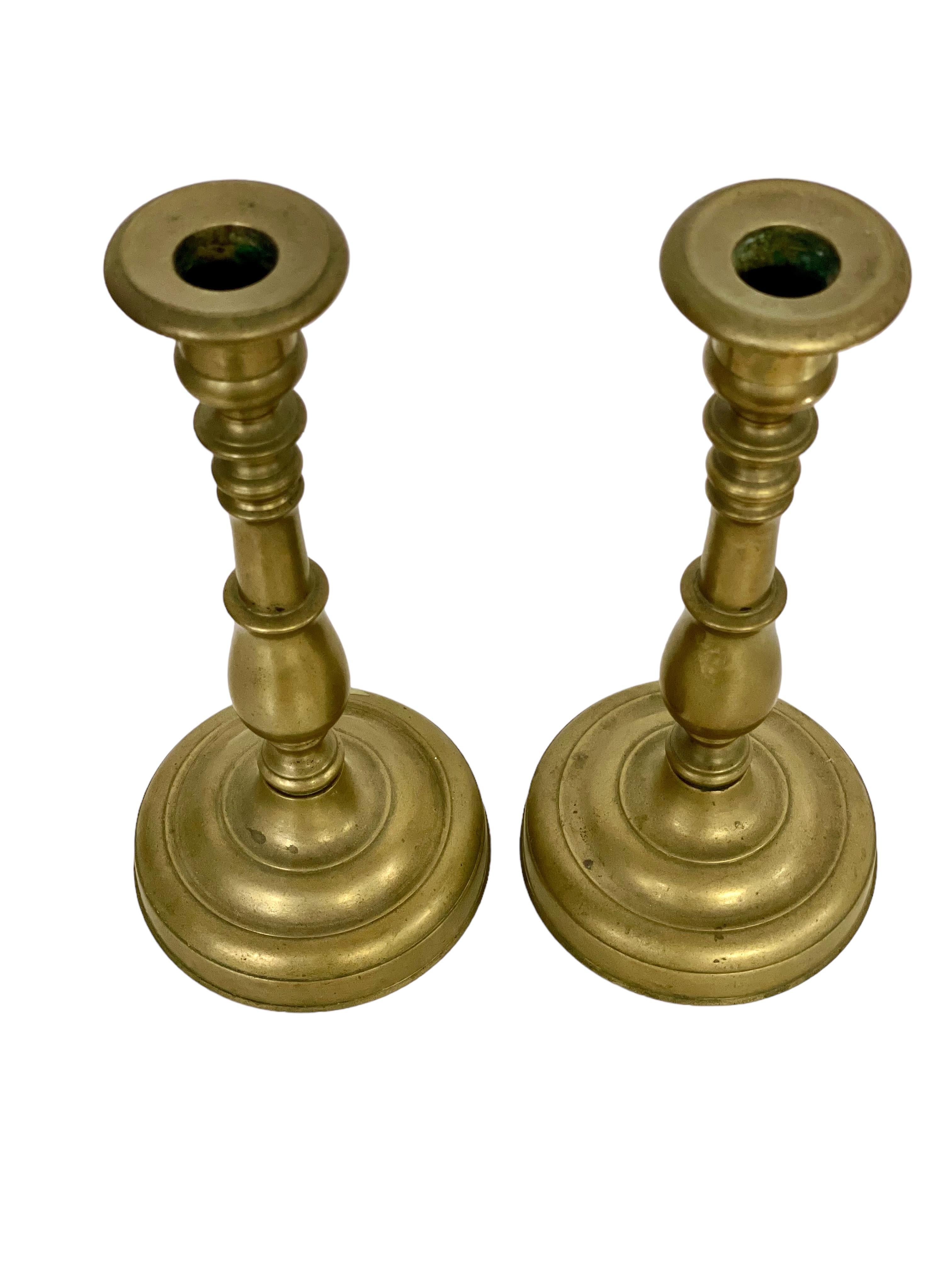 A simple and elegant pair of 19th century French “Flambeaux” gilt bronze candlesticks crafted in a traditional baluster form, rising above a heavy circular base. The turned and knopped stem terminates in a well shaped capital and wide, flared