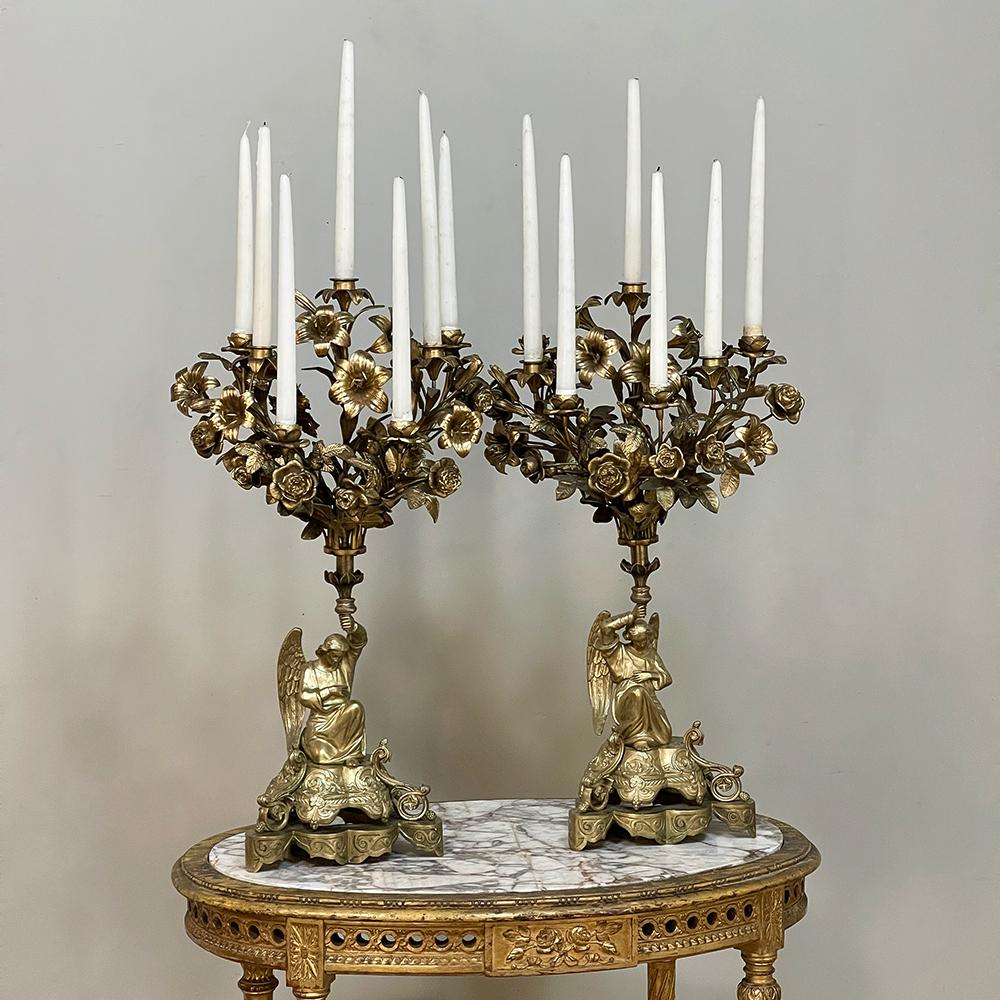 Pair 19th Century Bronze Candlesticks with Angels hail from the Napoleon III Period, and feature stunning angels on elaborately detailed tripod bases acting as caryatids for the candelabras above, each depicting a floral bouquet in full bloom.  The