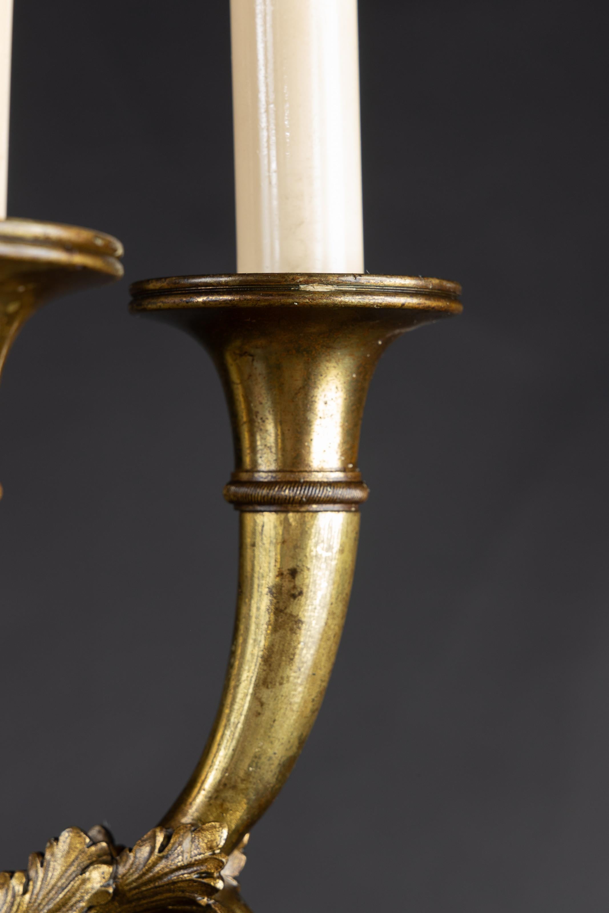 This pair of French Empire sconces are made of bronze and date back to the 19th century. The pair features a beautiful large torch back-plate with a floriate design at bottom, as well as horn-shaped bobeches. Each arm is adorned with acanthus