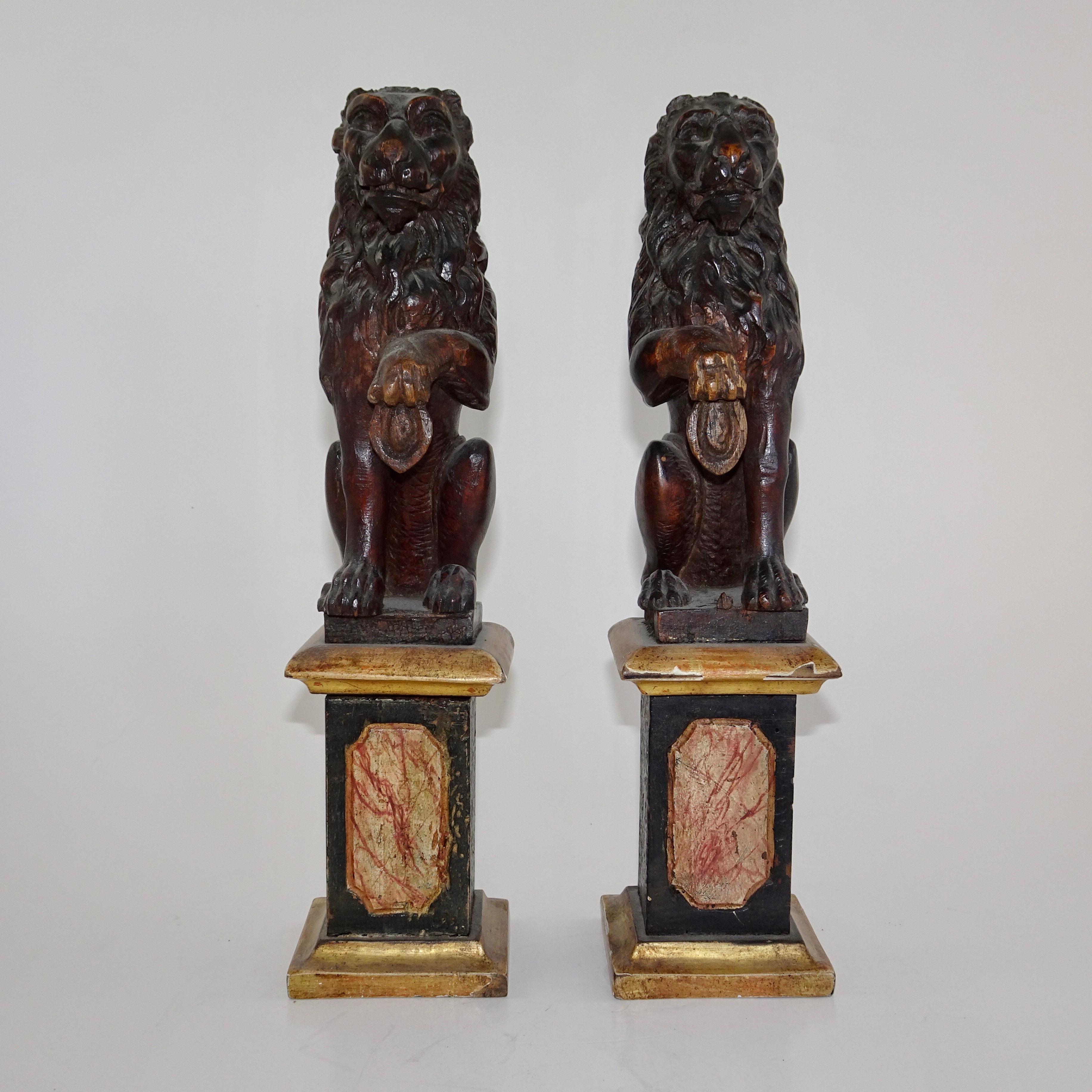 Pair of antique wood carved Lion Statues on Faux marble bases. The lions are depicted sitting on their hind legs with one paw lifted. The marble base is in shades of gold, red, and black.