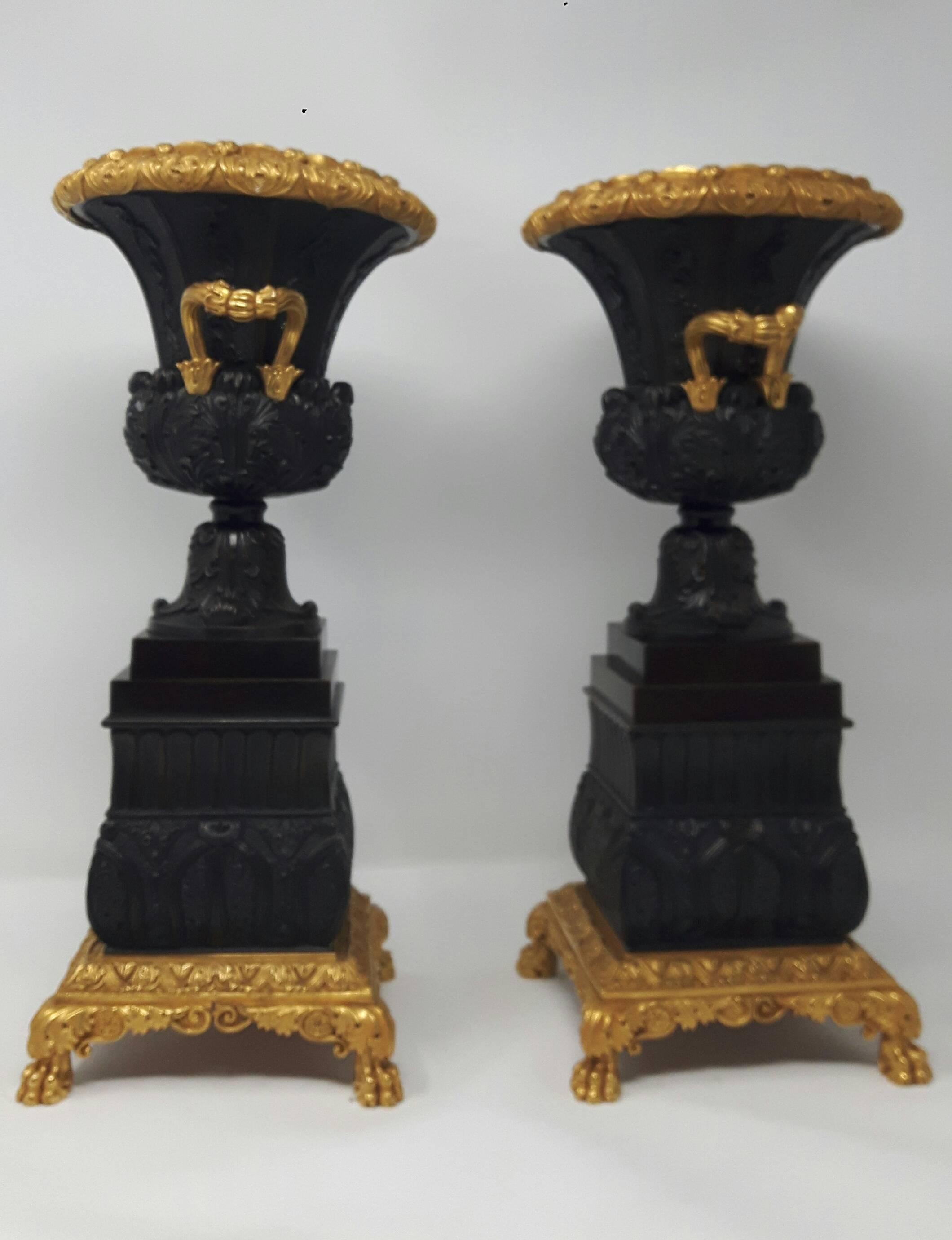 A delicately cast pair of twin handle bronze and ormolu urns in neoclassical style with deep moulded acanthus leaf design and garland of flowers, the entirety resting on gilded lion paws.