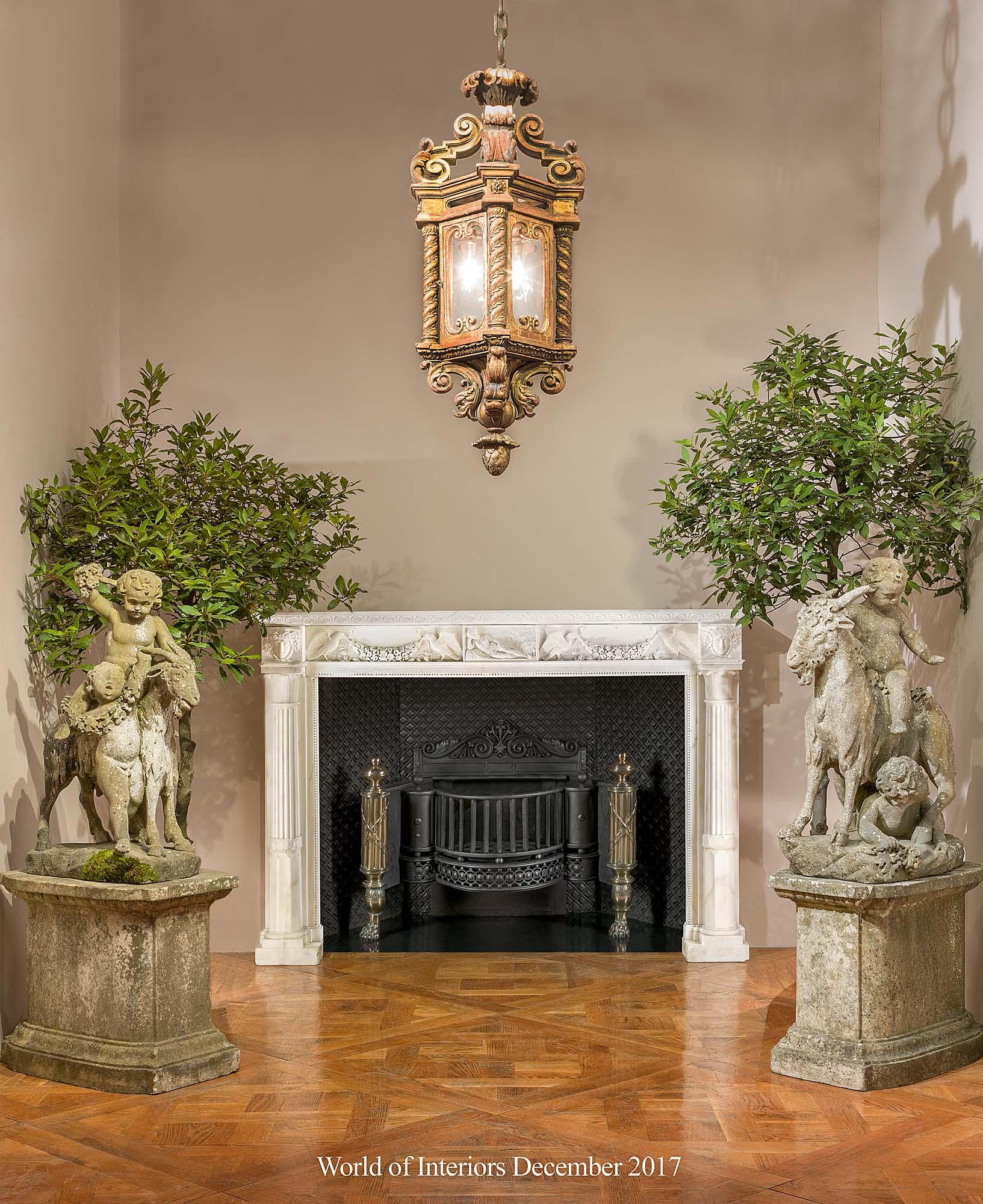 A pair of large 19th century Carrara marble Italian garden sculptures of playful Putti riding and cavorting with Billy Goats, holding aloft bunches of grapes and garlands of vine leaves and standing on rusticated bases mounted on the original