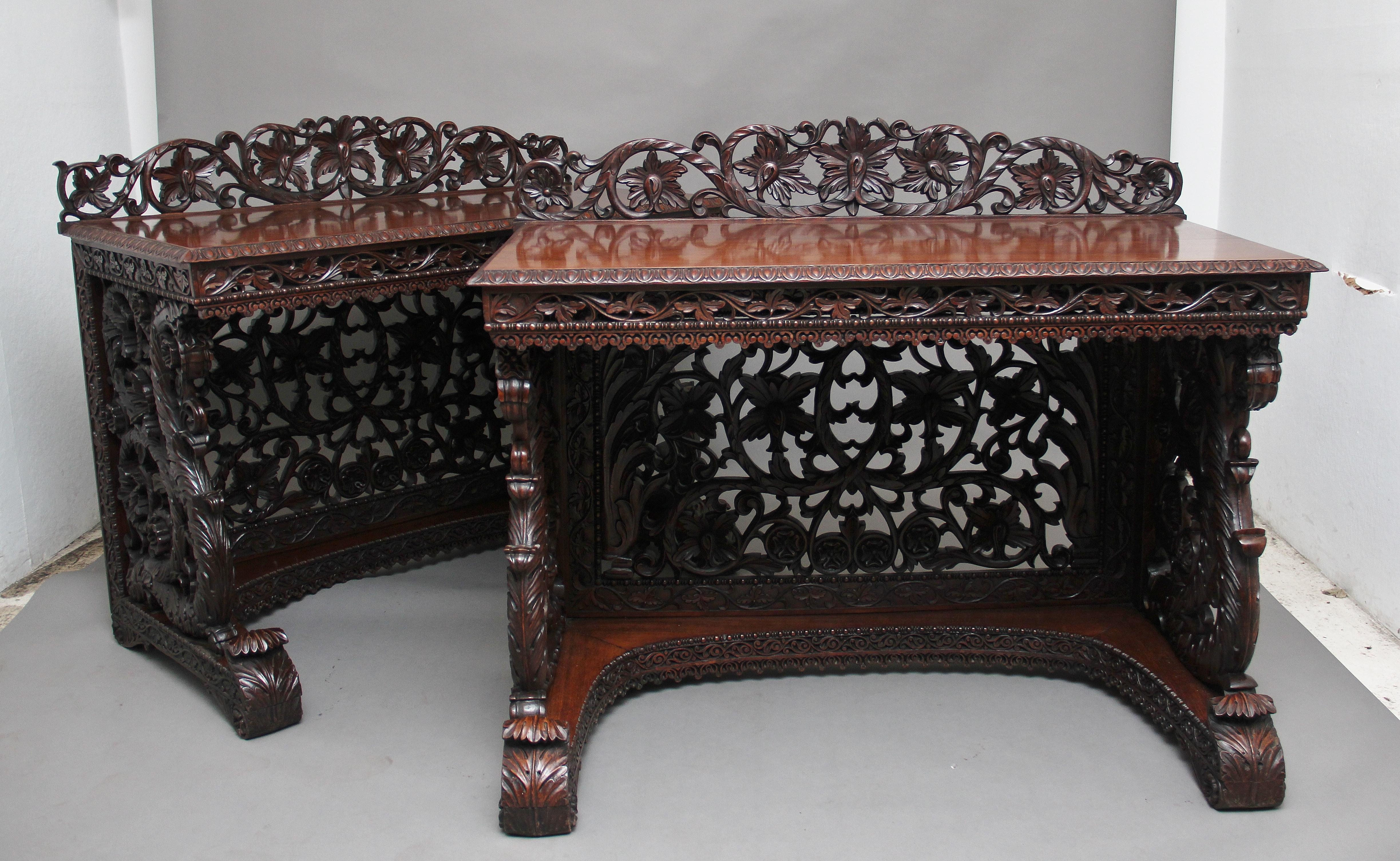 A superb pair of 19th century Indian carved console tables, each having a foliate scroll-carved pierced back over a rectangular top with ovolu-moulded edge upon pierced foliate scroll frieze, scroll apron and well carved conforming sides and back,