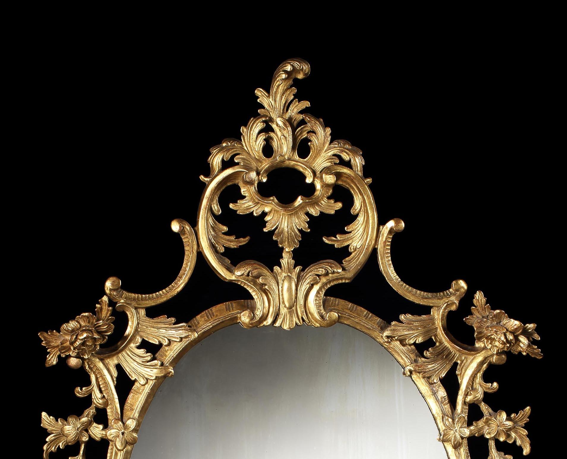 A good pair of looking glasses
In the manner of Thomas Chippendale

The oval mercury glass plates housed within ornate rococo carved and pierced gilt wood frames, composed of 'C' scrolls, flowering branchwork, and stylised acanthus