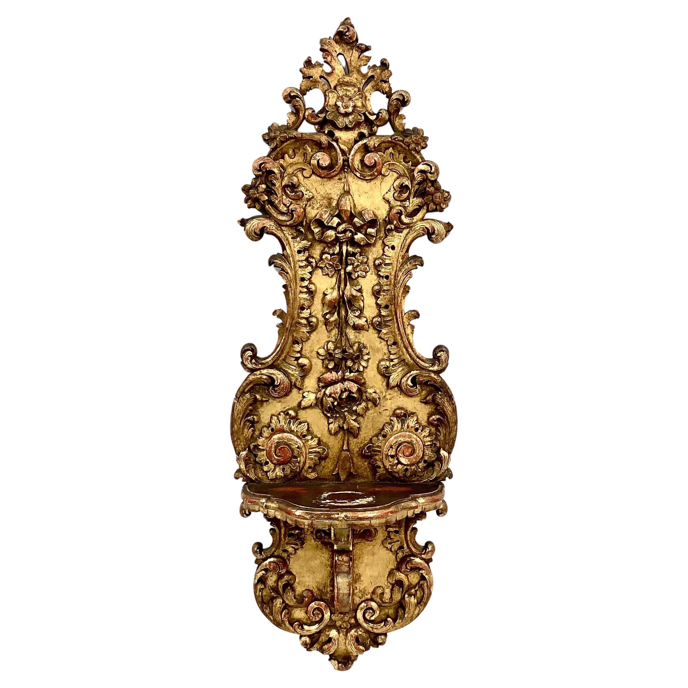 Unique pair of tall giltwood 19th century French wall brackets. Ornate scrolling, ribbons and floral motif throughout. Six inch shelf on each for displaying vases, candles, or other small items. Hanger in place on back. Wonderful, aged patina.