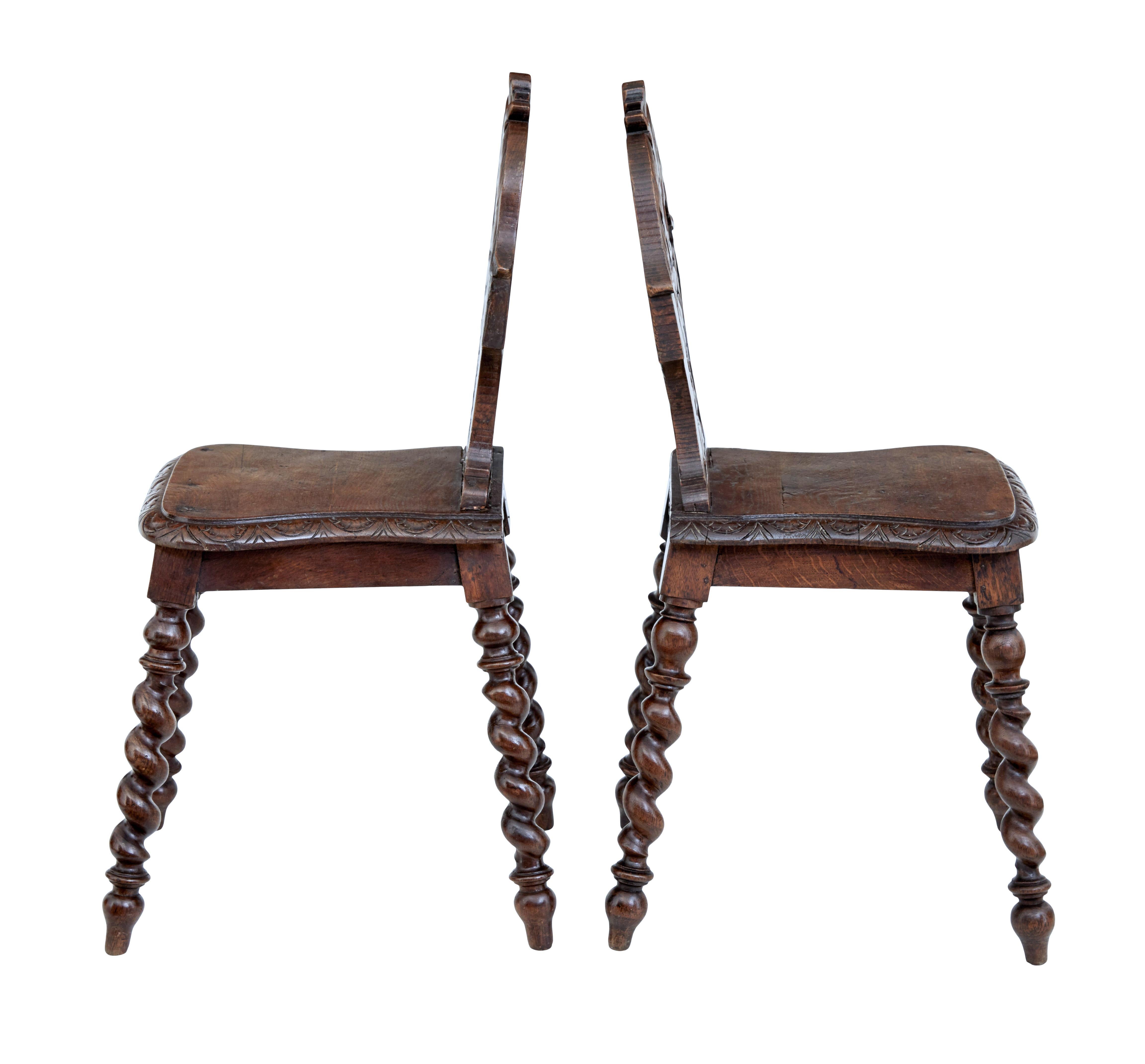 Pair of 19th century carved oak hall chairs circa 1880.

Carved back rests adorned with acanthus leaves and a central shell, linked to a shaped seat with further carved detailing. Standing on turned barley twist legs.

Later metal support to 1