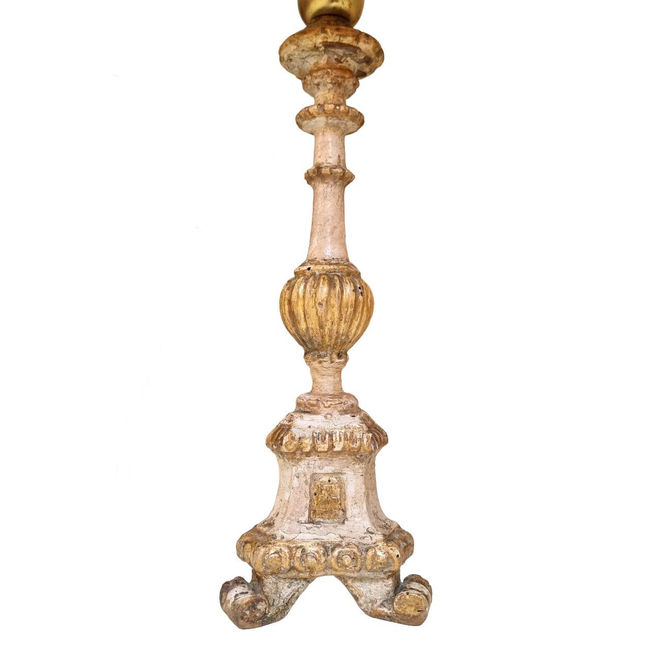 This is an absolutely fabulous pair of Italian carved wood candlesticks converted to table lamps, early 19th century, painted with ivory lacquer and finished with original gold leaf gilding.
Each candlestick stands on a tripod base ending with