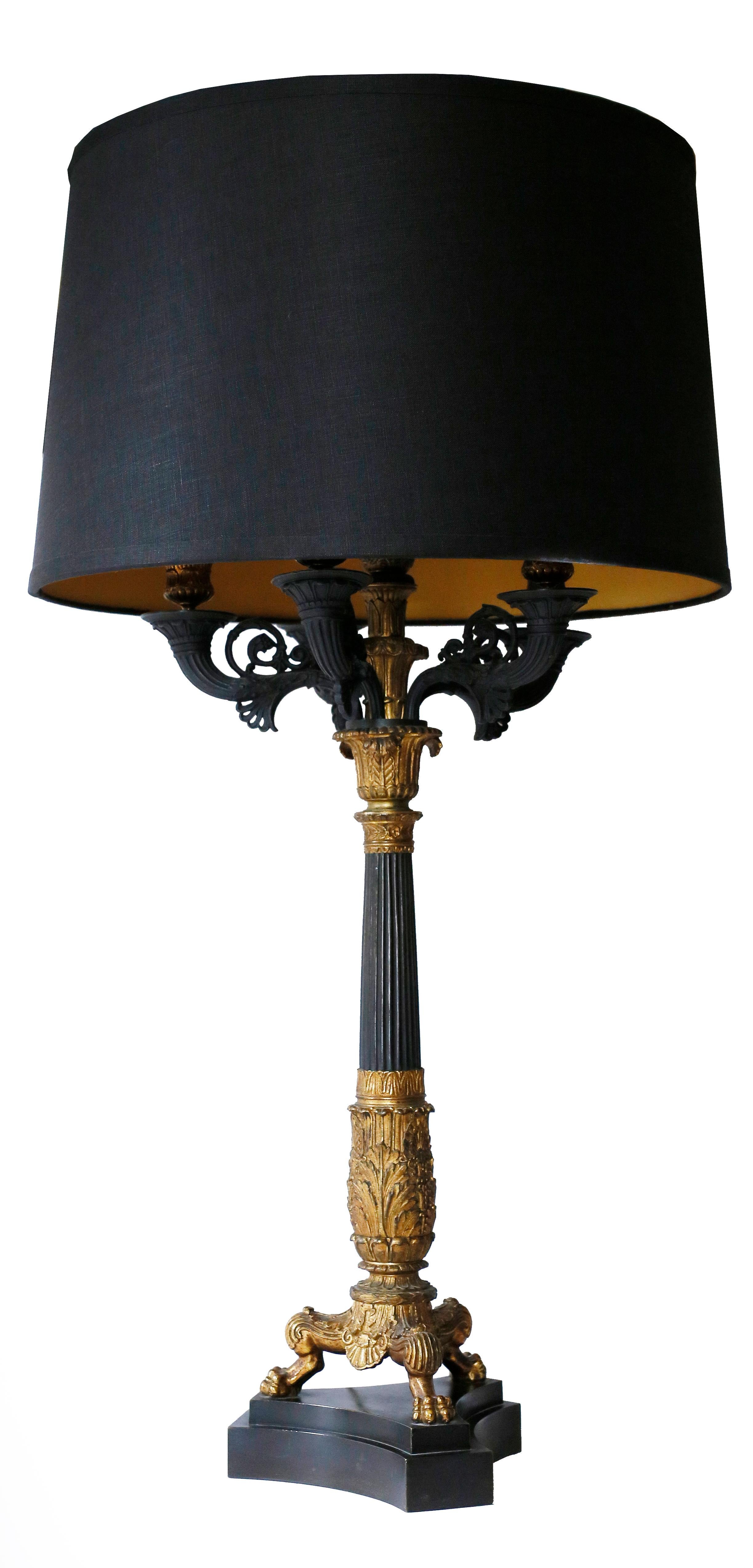 A fine pair of baluster neoclassical lamps of patinated bronze with gold detailing. A black basalt stone base supports a paw-footed tripod with a baluster detailed with fluting and acanthus. The five light candle supports exhibit scrolls and bronze