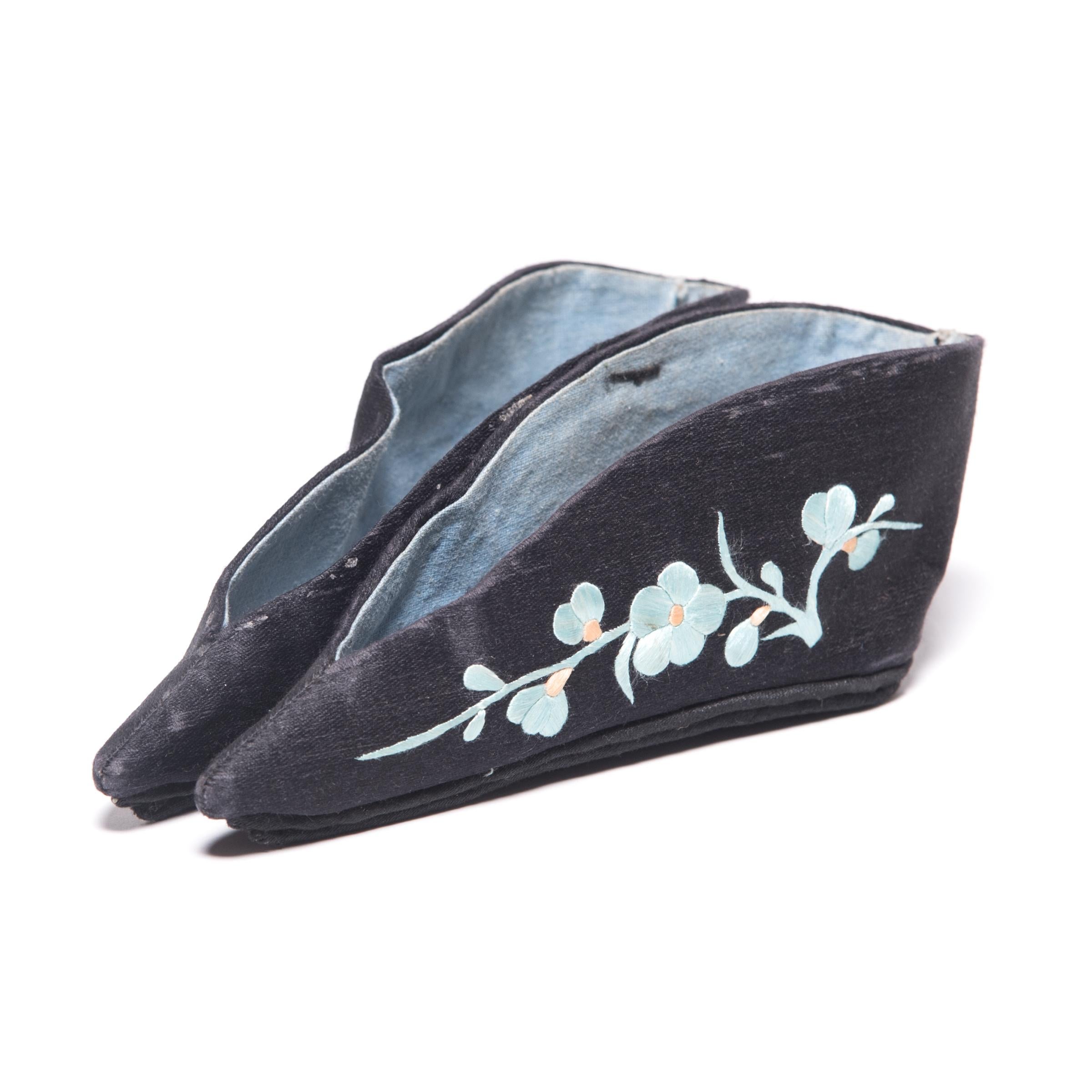 These pointed slippers, beautifully embroidered with light blue plum blossoms on black silk, were shaped to resemble a lotus bud and enhanced the diminutive shape of bound feet. A practice that began in the Tang dynasty and reached the height of its