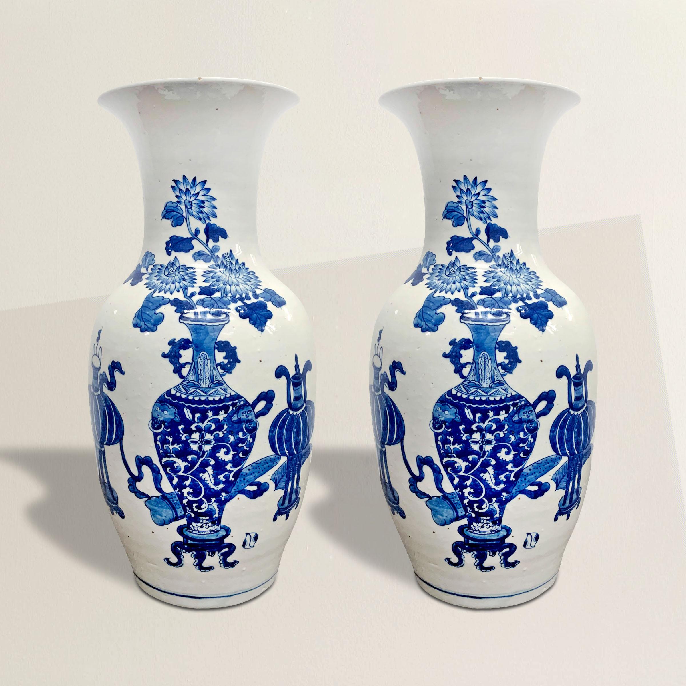 A pair of 19th century Chinese blue and white vases each hand-painted with various scholar's objects including vases filled with chrysanthemums, and flanked by pairs of incense burners, and scrolls behind the vases.