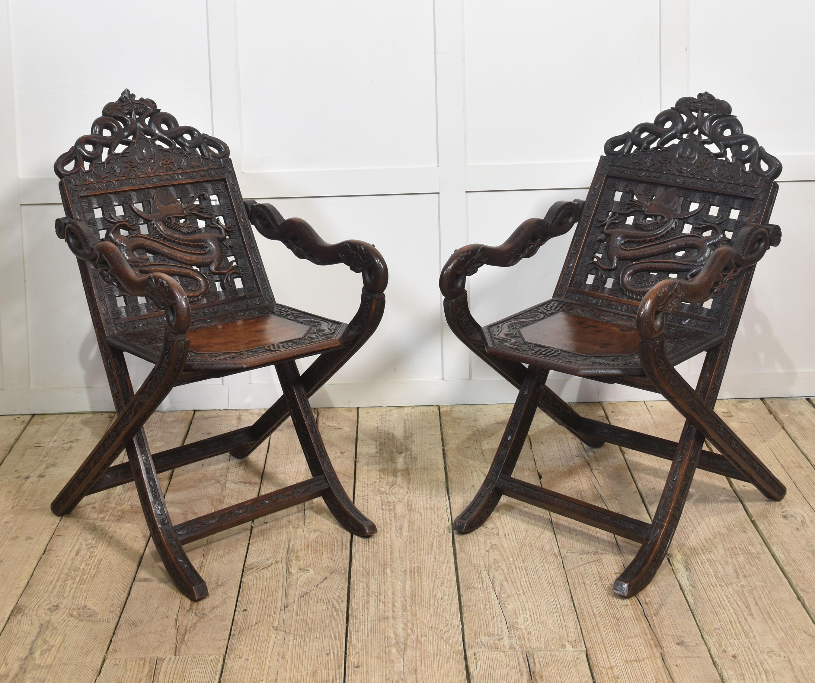 Pair of 19th-century Chinese folding armchairs, the arched backs profusely carved and detailed with dragons to the solid seat with further carved decoration.Flanked by shaped arms depicting serpents. All raised on square supports united by