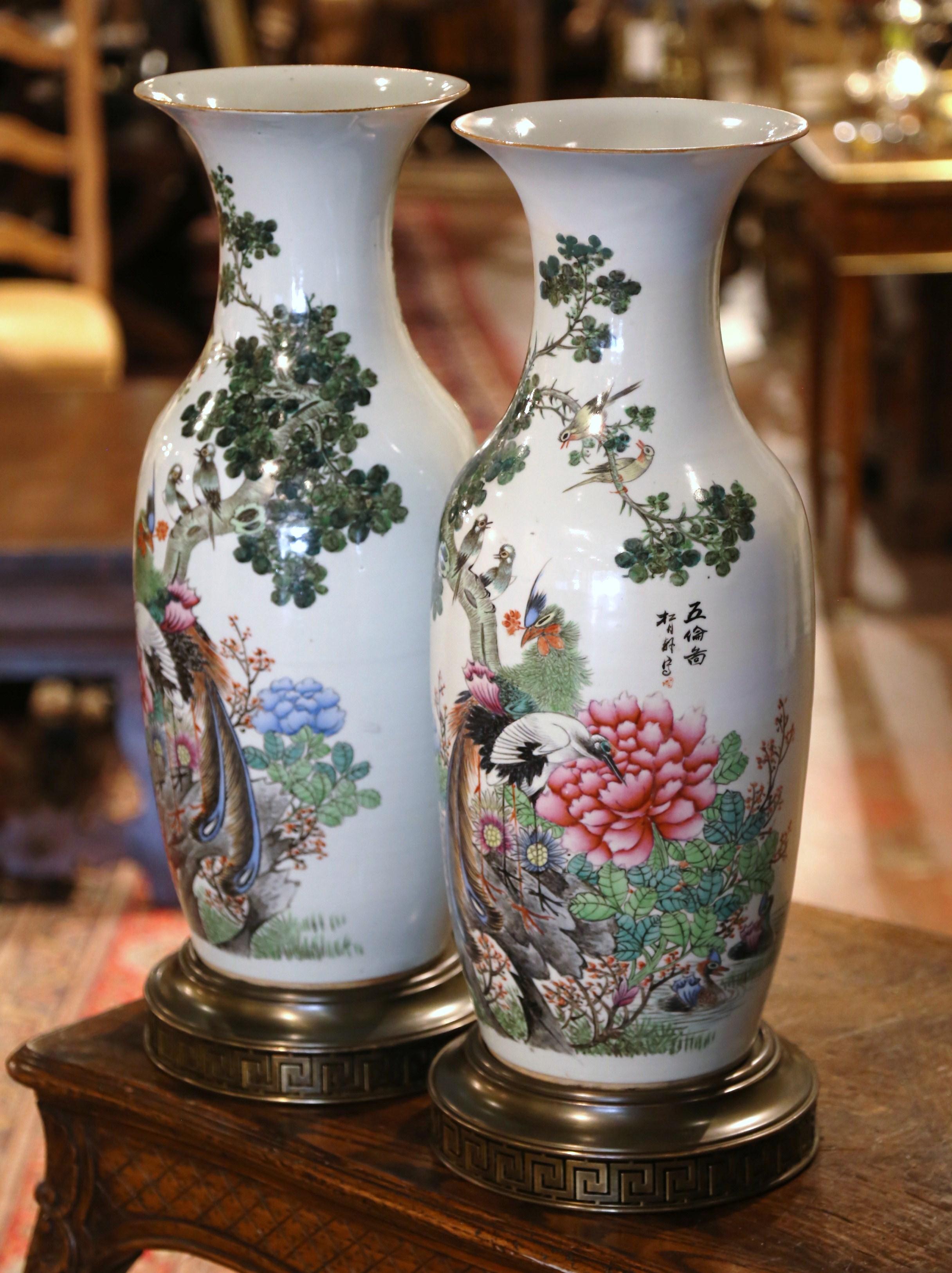 These elegant colorful antiques vases were created in China circa 1870. Standing on platform brass bases, the large vessels feature a flared rim and tapered body. Each body is decorated with hand painted garden scenes depicting birds, wildflowers,