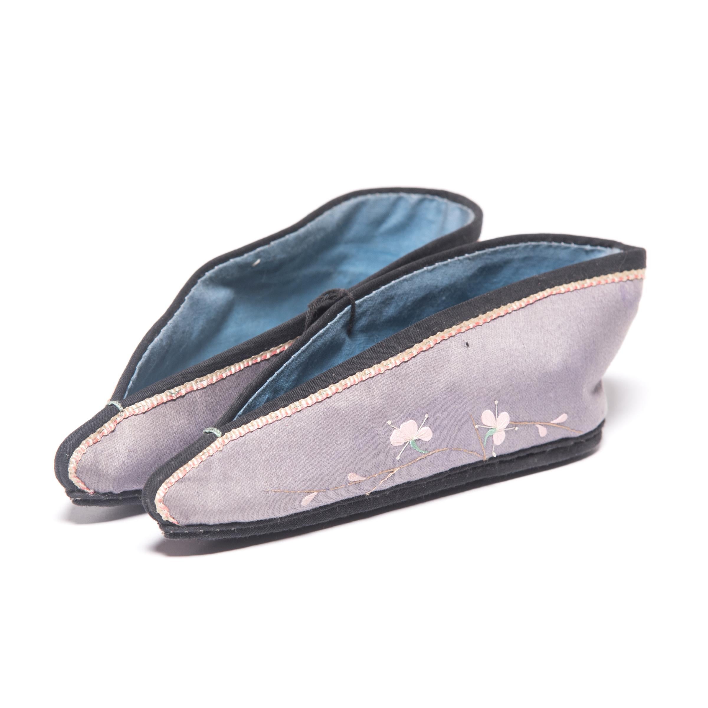 These pointed silk slippers, beautifully embroidered with pink plum blossoms, were shaped to resemble a lotus bud and enhanced the diminutive shape of bound feet. A practice that began in the Tang dynasty and reached the height of its popularity