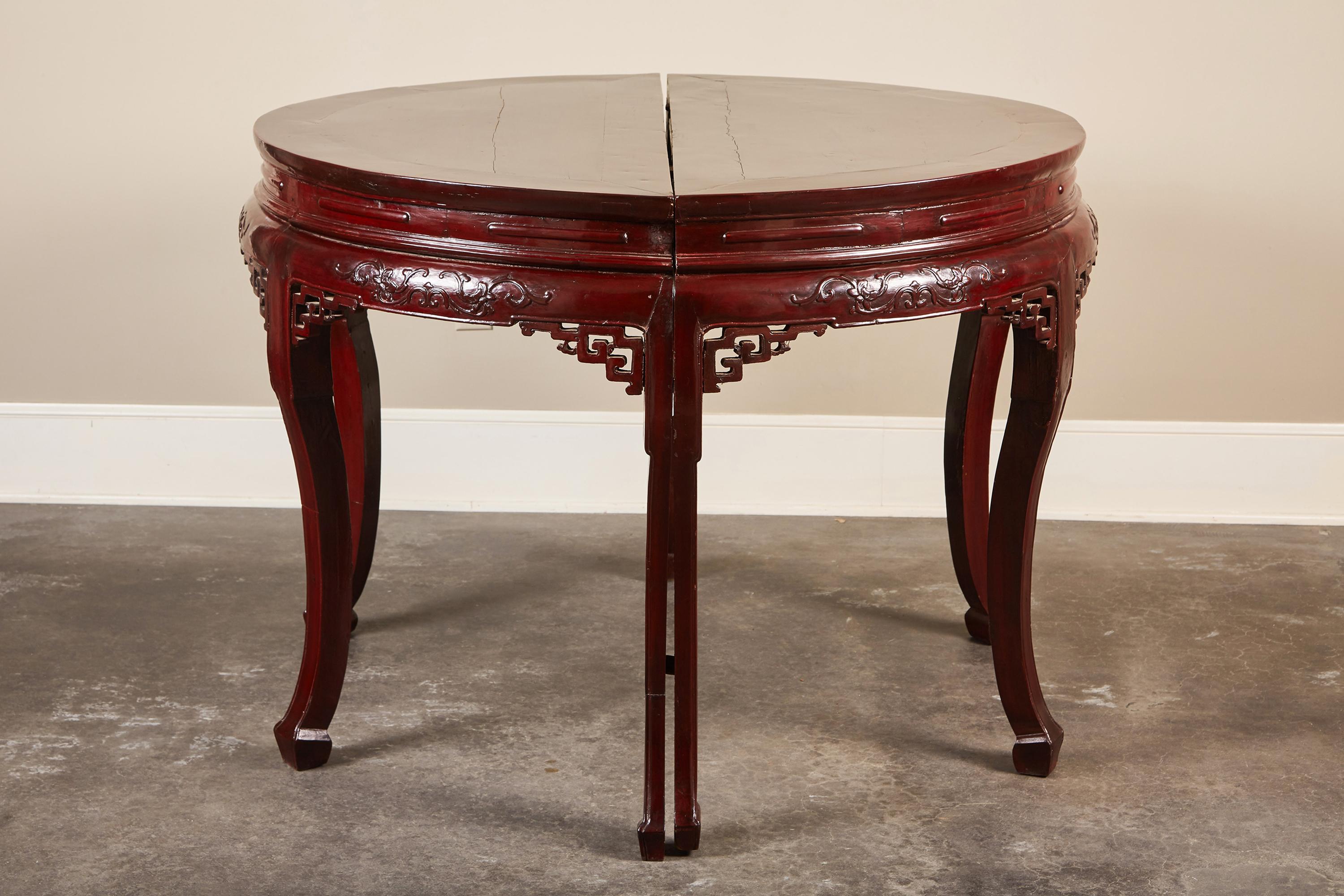 Pair of Chinese Qing Dynasty demilune tables made in the 19th century. Covered in deep maroon lacquer and featuring delicate relief-carved scrolls along the apron, intricate pierced spandrels and molded S-form legs with hoof feet, these versatile