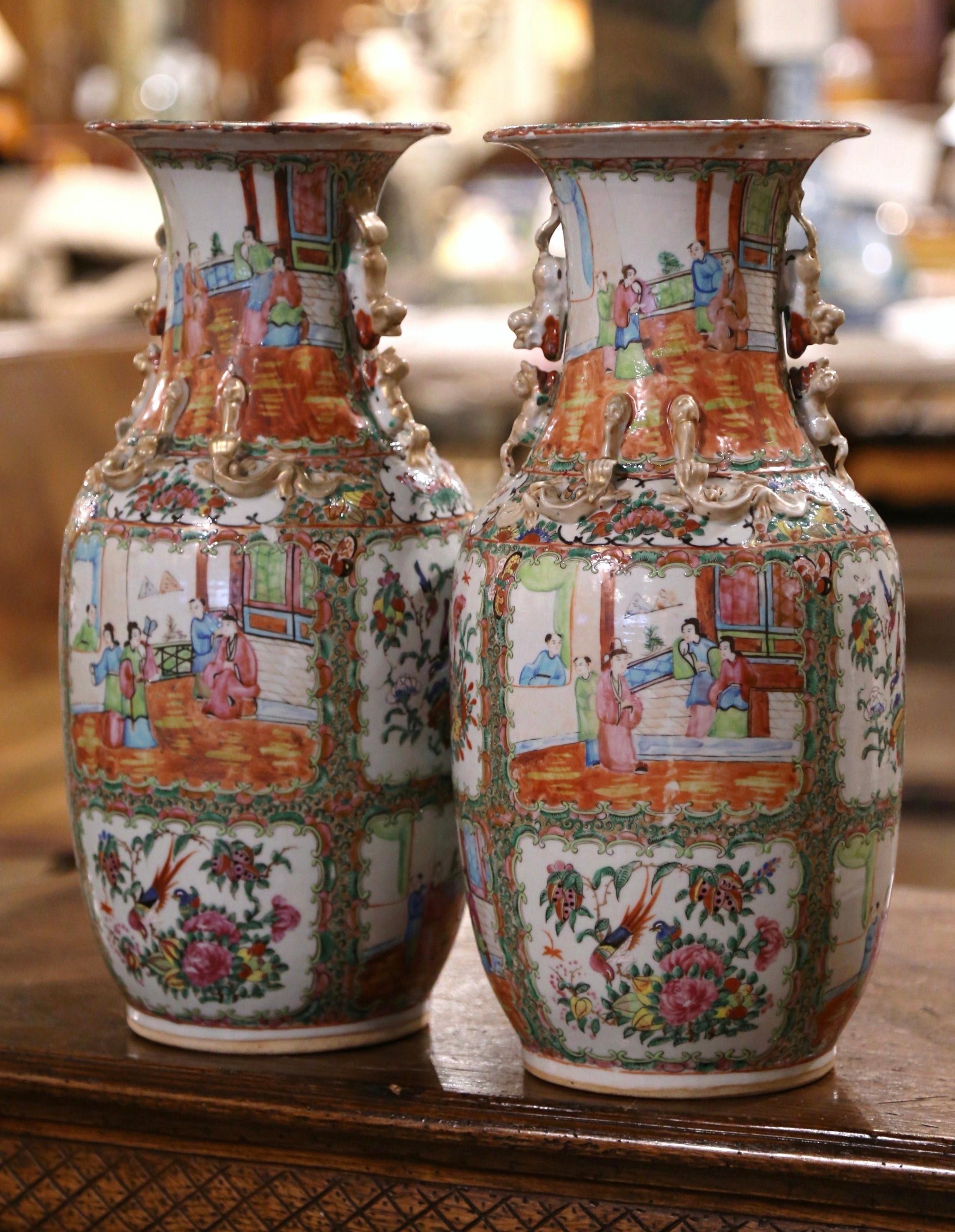 These elegant Famille Rose Imperial Canton vases were created in China circa 1880. The tall vessels made of porcelain feature a tall and wide neck; the are dressed with dog figures in high relief and embellished with gilt lizard motifs. Each vase is