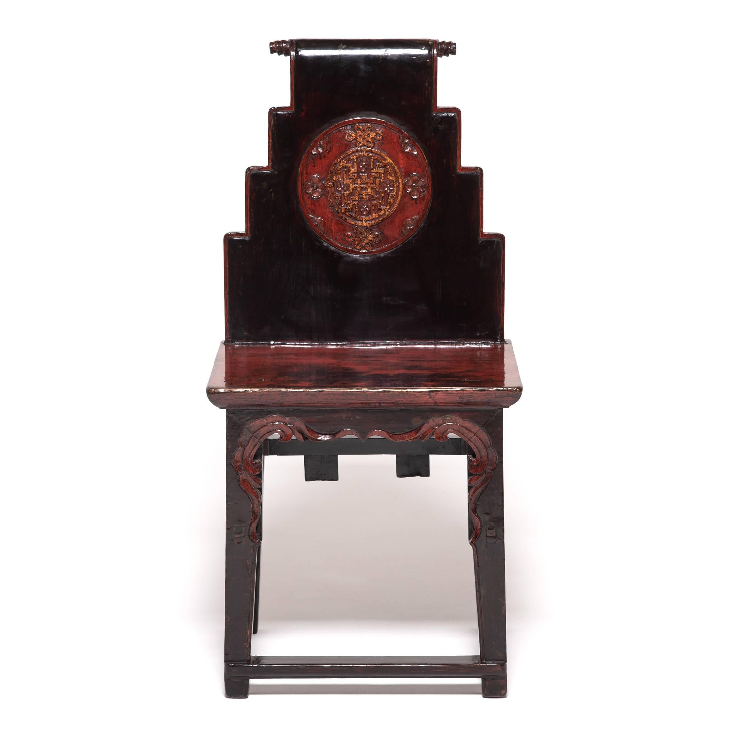 This pair of 19th century Chinese black-lacquered chairs are carved with ornate, red-lacquered aprons and stepped backs ending in a simple, elegant scroll. The round medallions carved into the chair backs are lacquered and gilded, depicting Buddhist