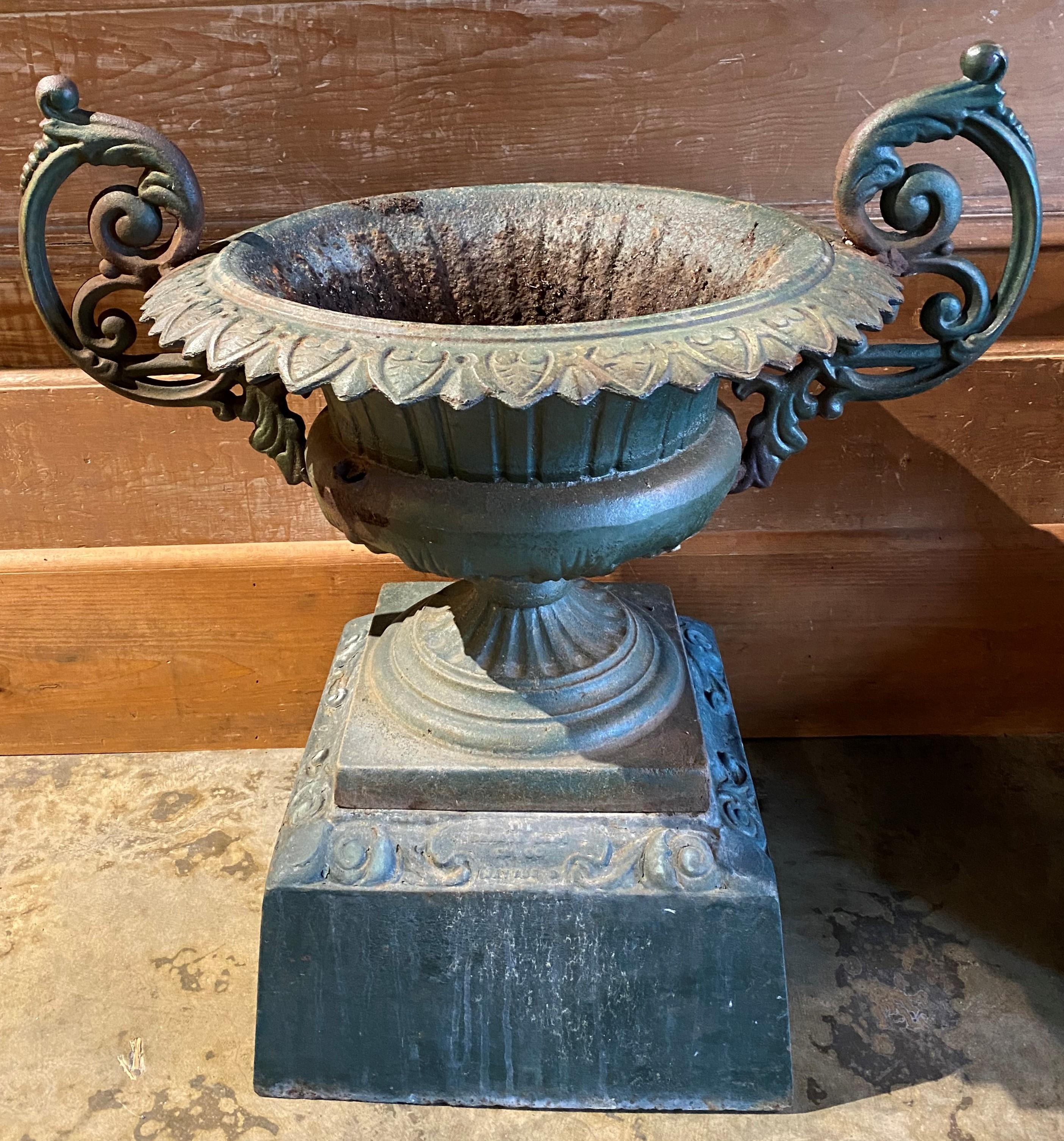 A fine pair of classical form urns with C-scroll handles in old green paint, petal rims, signed “Kramer Bros Fdy Co, Dayton, O,” each urn with separate scroll decorated base. The Kramer Bros Foundry was founded in 1895 in Dayton, Ohio. The pair