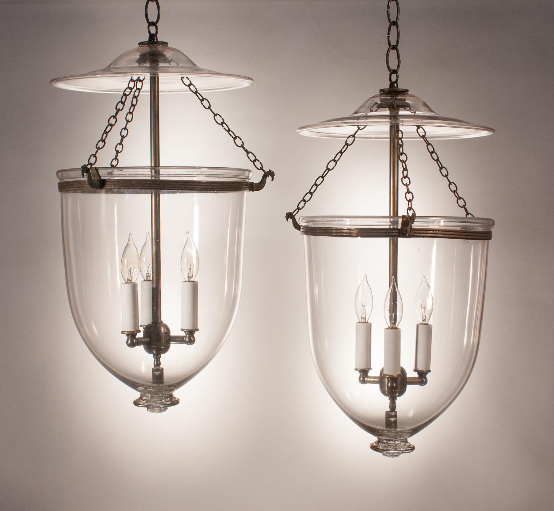 An outstanding pair of bell jar lanterns, circa 1870, with original rolled brass bands. The quality of the clear, hand blown glass is excellent, and the glass pontil bases have a nice spiral pattern. The set is very well-matched pair and has