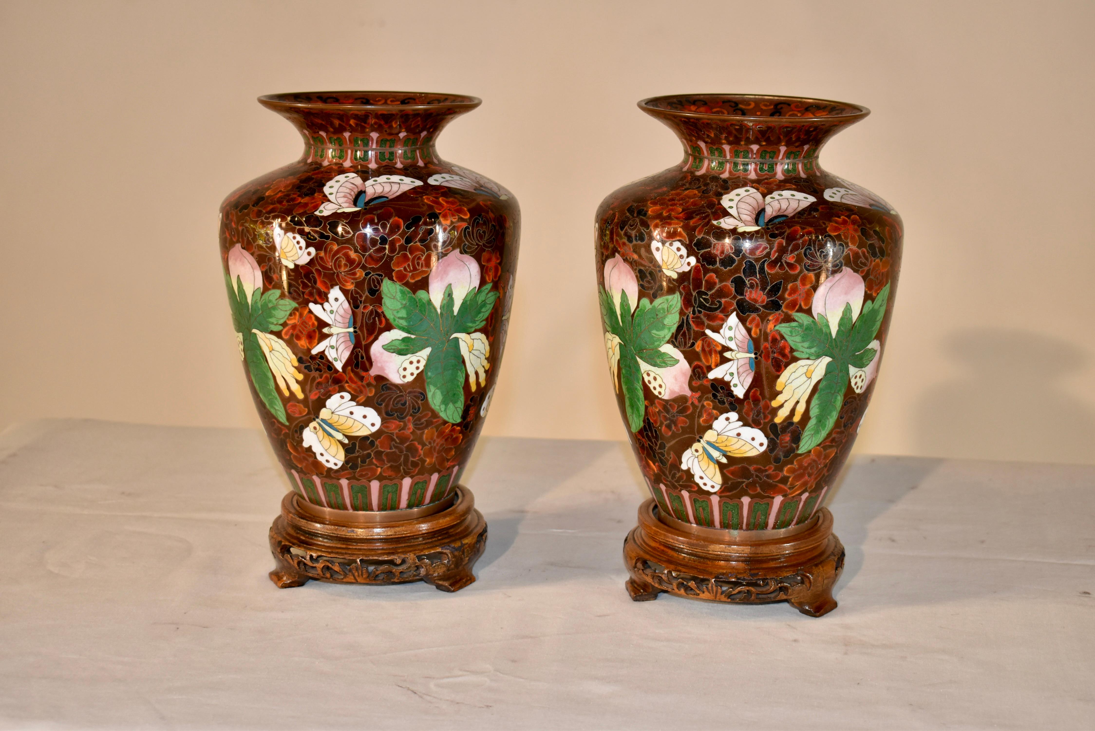 Pair of fantastic 19th century cloisonné vases in fabulous reds, browns, greens and pinks. They have gorgeous floral decoration in vibrant greens and pinks with flitting butterflies all over the vases. They are supported upon hand carved and pierced