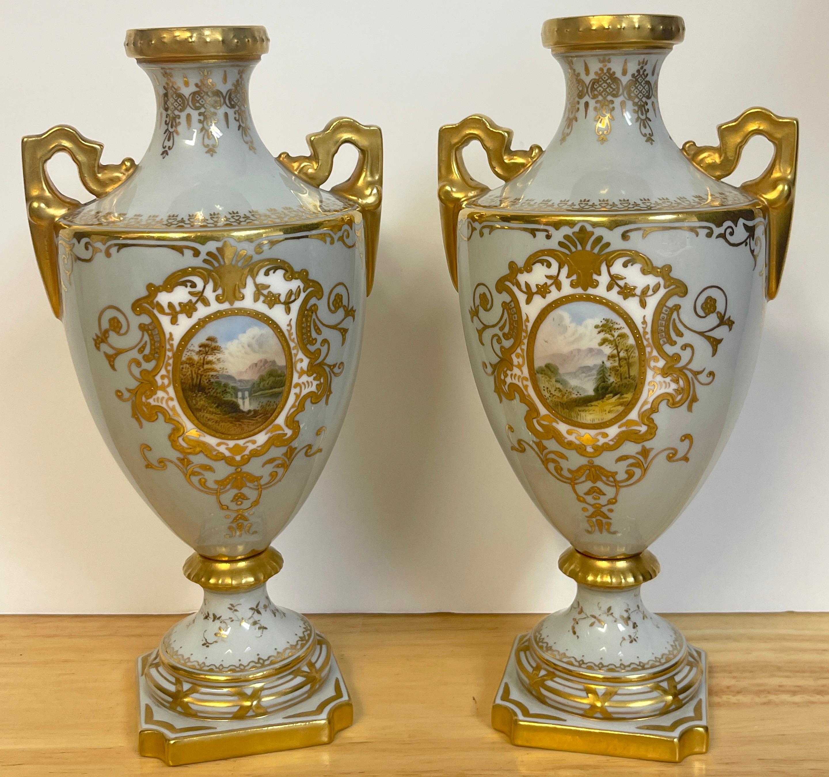Pair of 19th century Coalport scenic cabinet vases, each one with a blue-gray background, finely gilt and painted with oval landscape vignettes, raised on a canted square pedestal base.
  