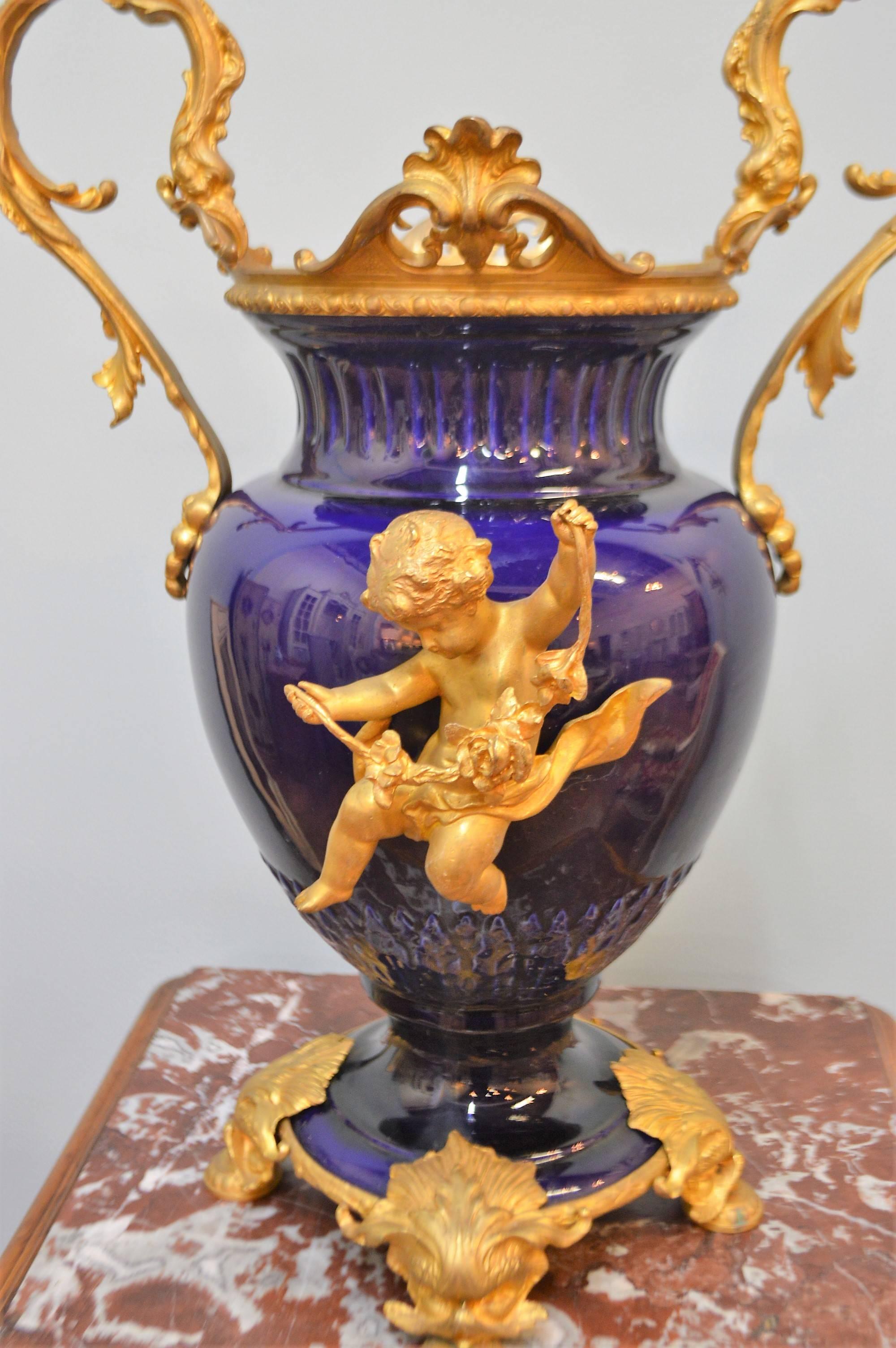 Exceptional quality on this pair of 19th century cobalt blue porcelain urns. The decorative bronze gilded elements represent cherubs, attractive large handles, feet and fine bronze upper rims.