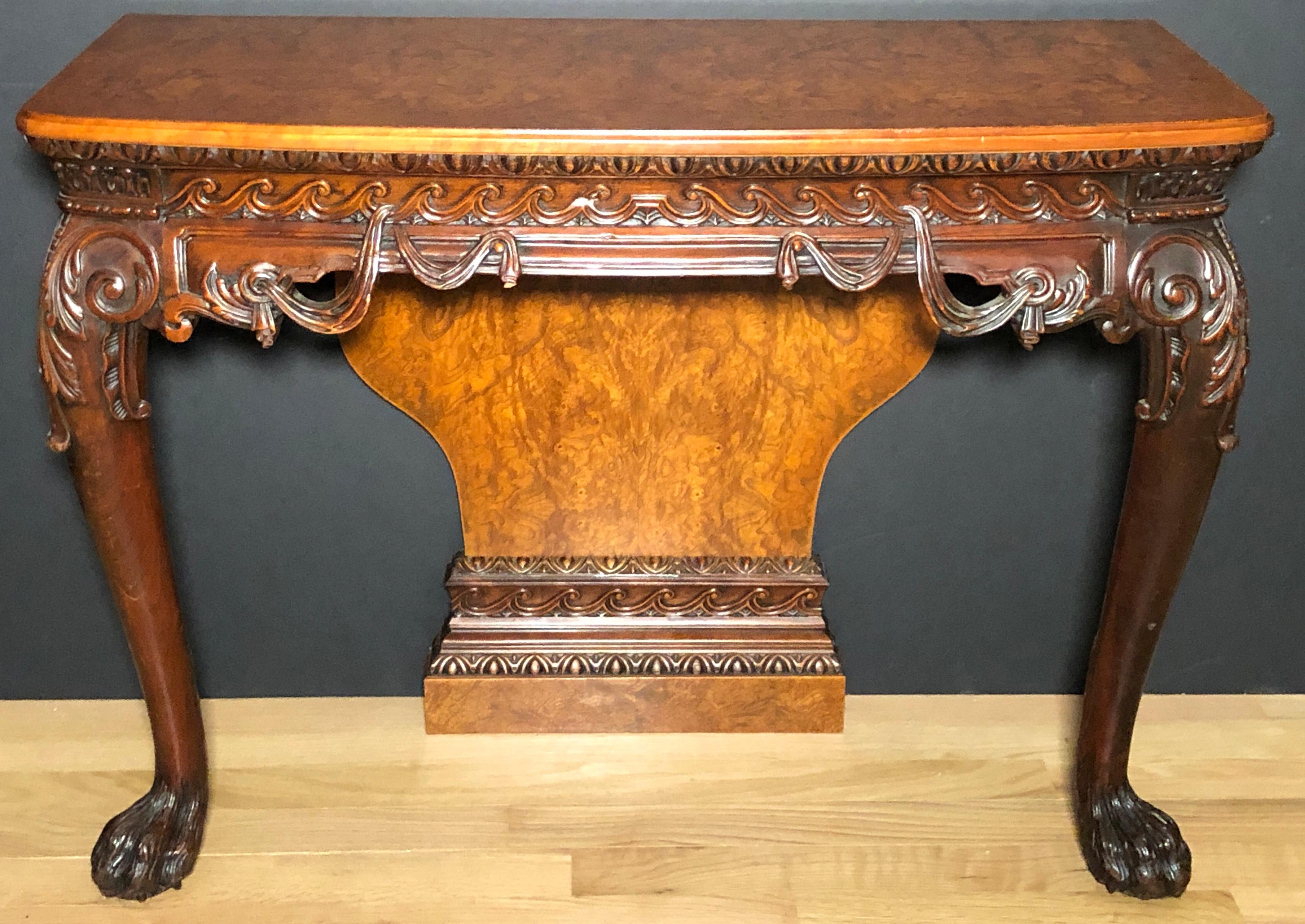 A fine pair of carved console tables manner of William Kent, 19th century carved console tables with bookmatched and crossbanded burl wood tops and backs. Carved gallery with swags and waves and acanthus leaves. With lion paw feet.