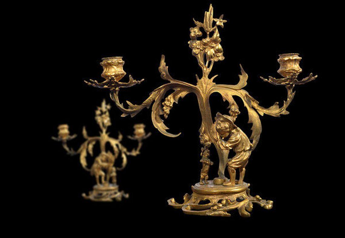 A pair of late 19th century continental two arm gilded metal candelabra.
The amusing scene each depicting a young boy with a small dog, the dog on its hind legs, the boy tapping a tambourine, both under a central stem displaying flora and