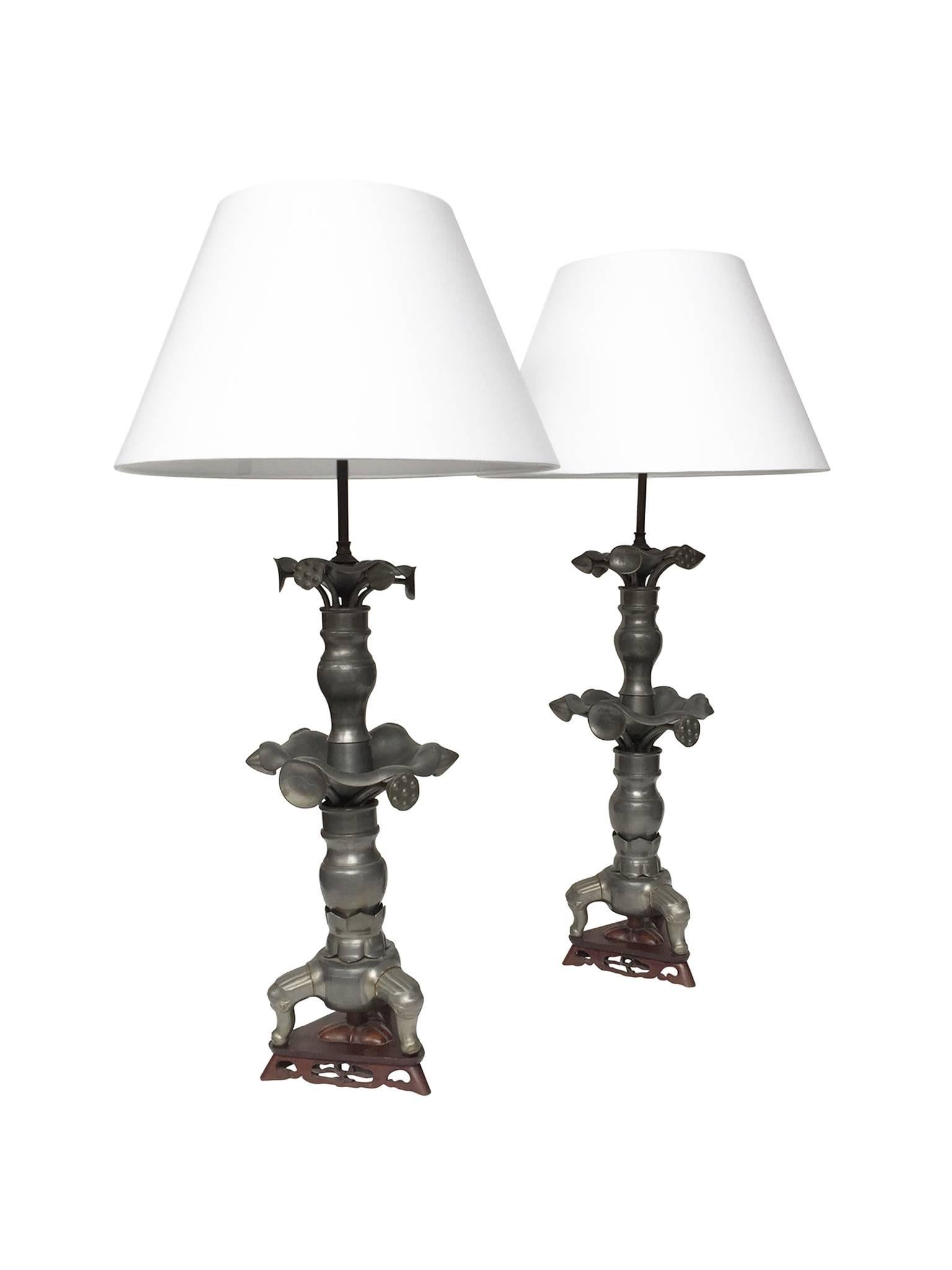 These lamps are comprised of 19th century pewter candlesticks that have been transformed into stunning table lamps. Their bases are carved wood with a warm red finish. The pewter bodies have undulating forms resembling petals and stems that radiate