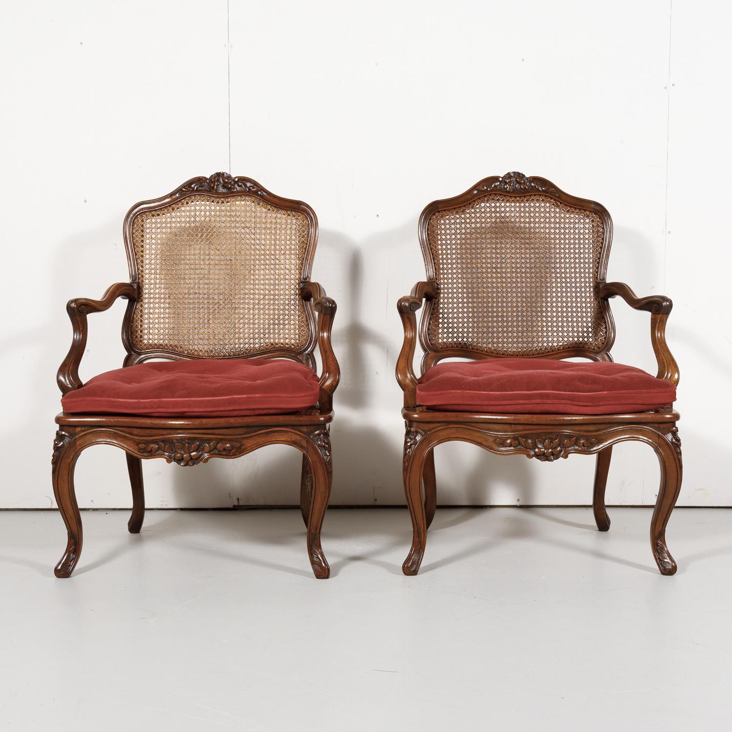 A lovely pair of 19th century Country French Louis XV style armchairs having solid walnut frames and cane seats and backs with removable loose cushions, and raised on elegant cabriole legs, circa 1890s. Each charming provincial armchair features