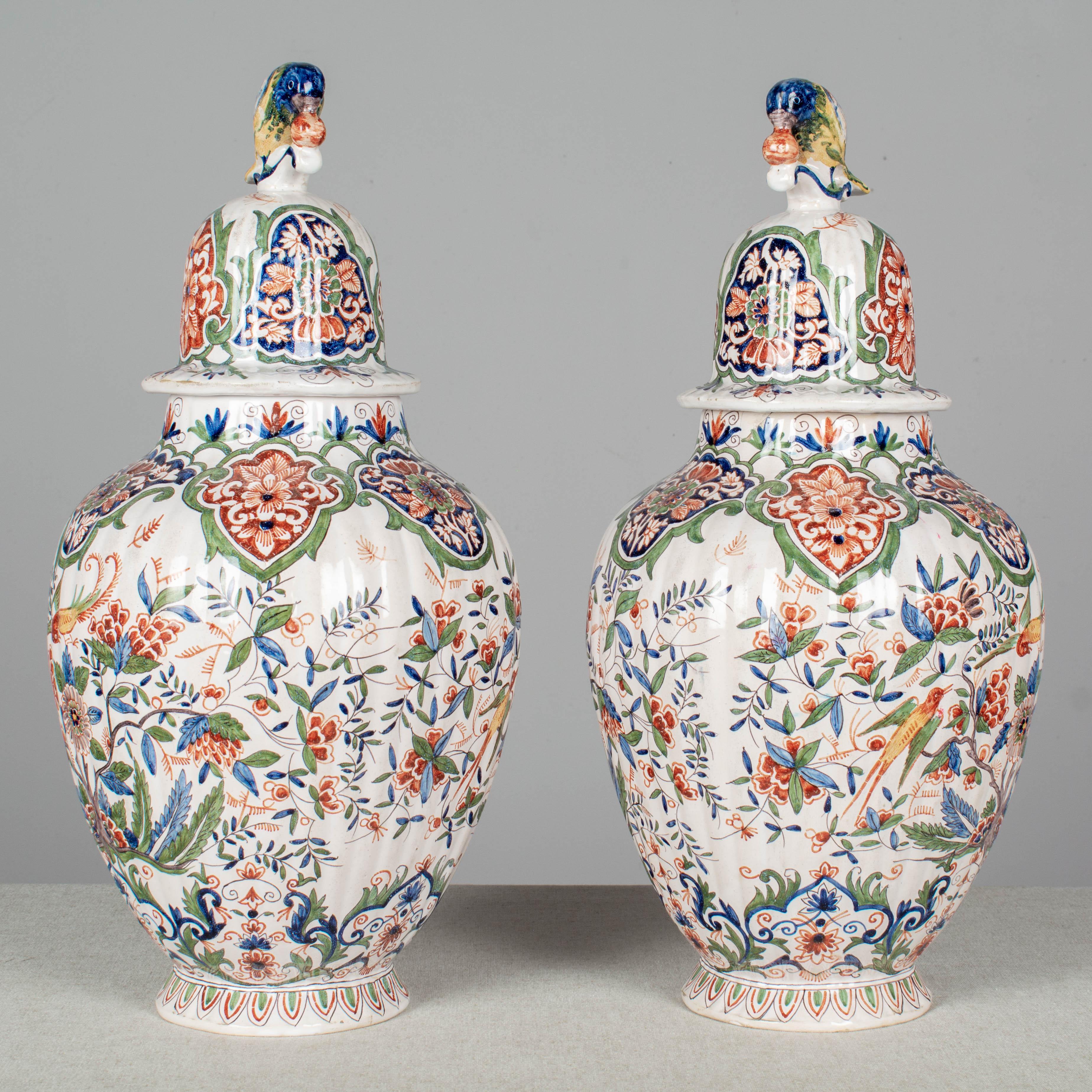 A lovely pair of 19th century Dutch polychrome painted delft faience urns, or ginger jars. Colorful hand painted decoration shows a pair of songbirds among stylized flowers in a palette of iron red, moss green, cobalt blue, bright yellow and orange.