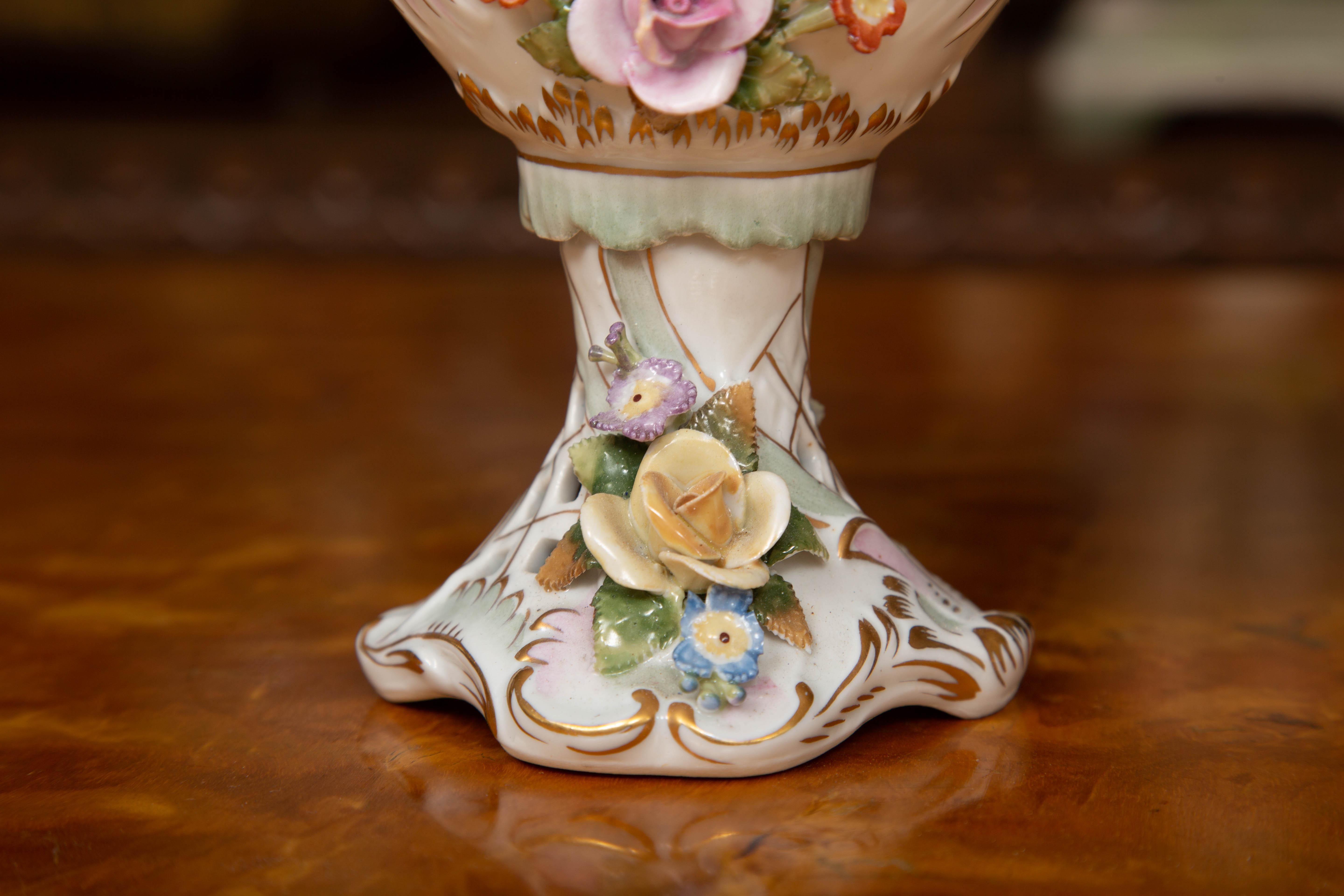 This is an elegant pair of German Dresden style potpourri vases, delicately painted overall with flowers and enhanced by clusters of porcelain flowers. The vases are lidded with a pierced top capped by a prominent finial of a cluster of porcelain
