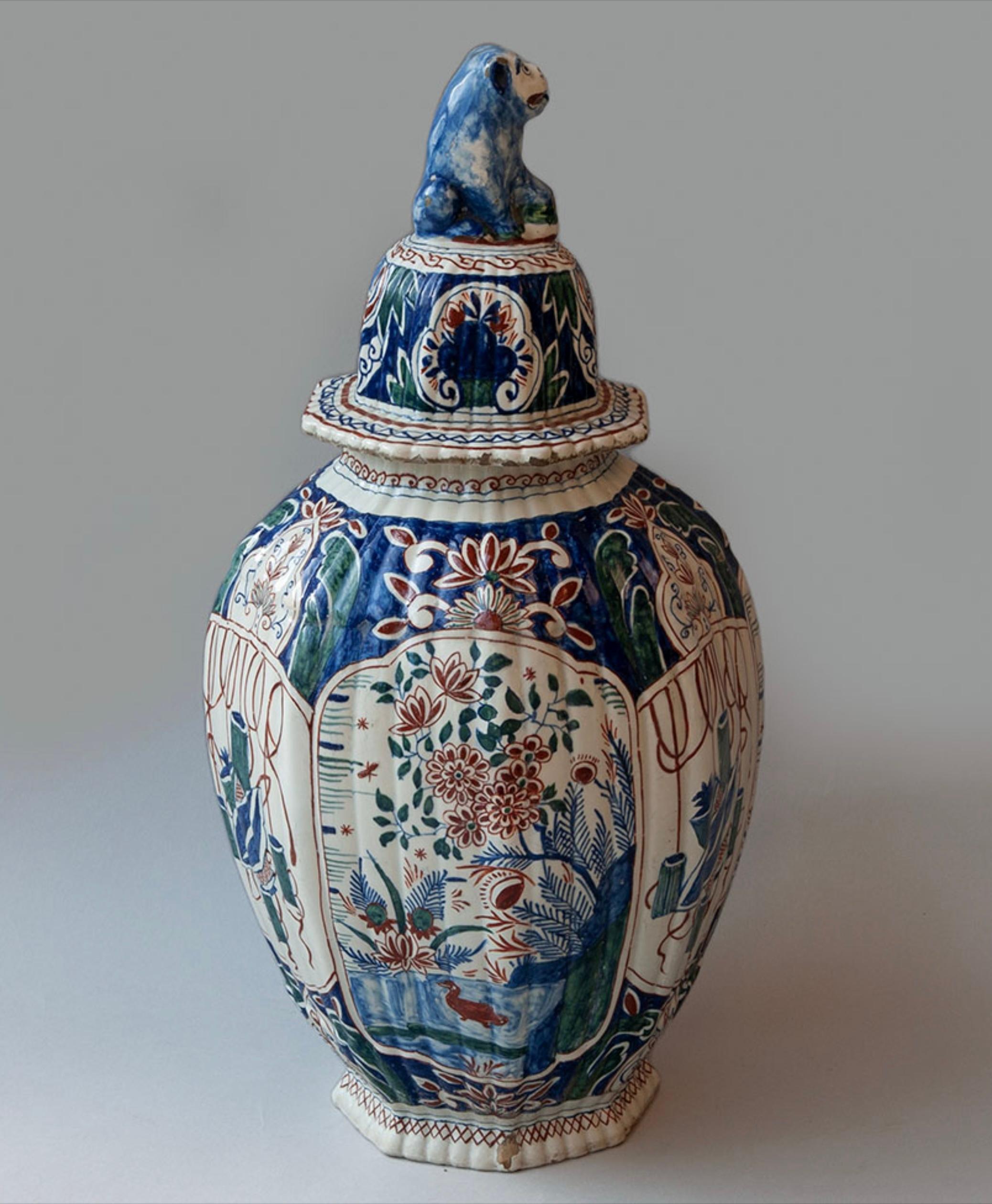 A fine pair of Delft polychrome lidded vases of hexagonal form, decorated in reds, blues and greens on a white ground with birds and flowers and stylised garden objects. The lids similarly decorated and mounted with Fo dog lion finials.