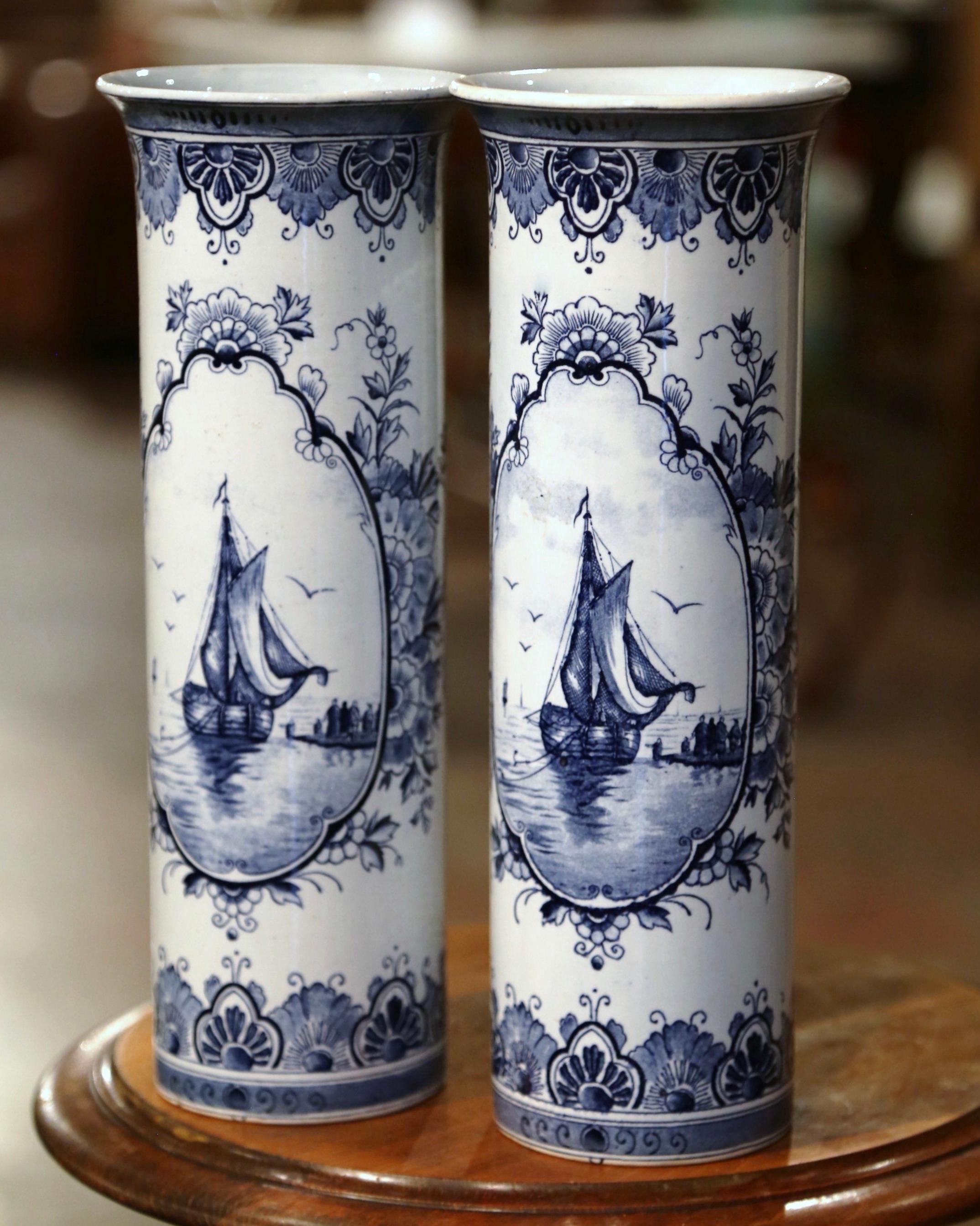 Decorate a shelf or console table with this elegant pair of antique vases with sailboat motifs. Crafted in Holland circa 1890, the round vases have a shell shape form with a wide rim at the top. Each vessel is hand painted in the blue and white