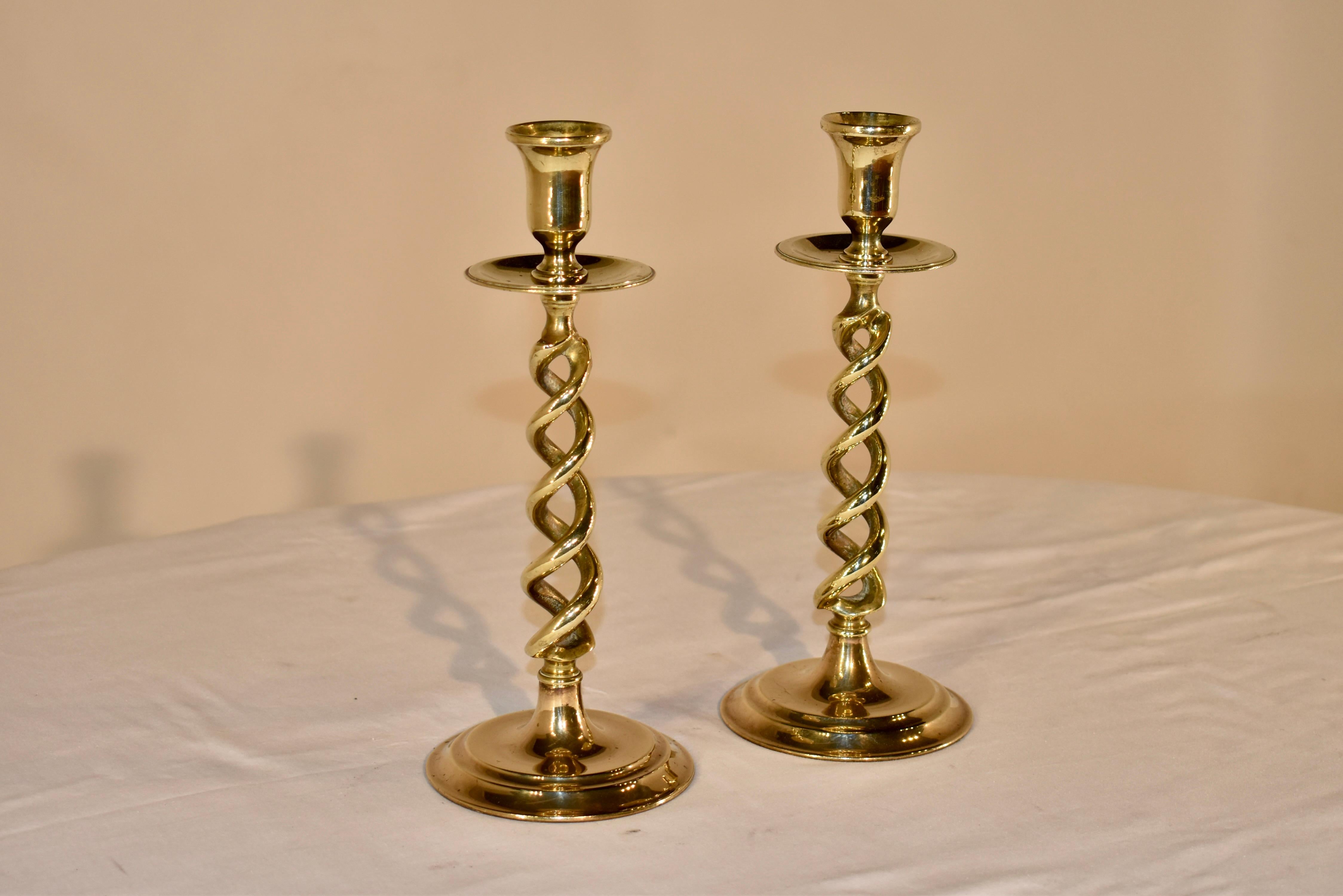 Pair of 19th century brass candlesticks from England. The candle cups are tulip shaped and are sitting on top of a large bobeche with rolled edges. The stems of the candlesticks are in and open barley twist design, and resting on top of turned