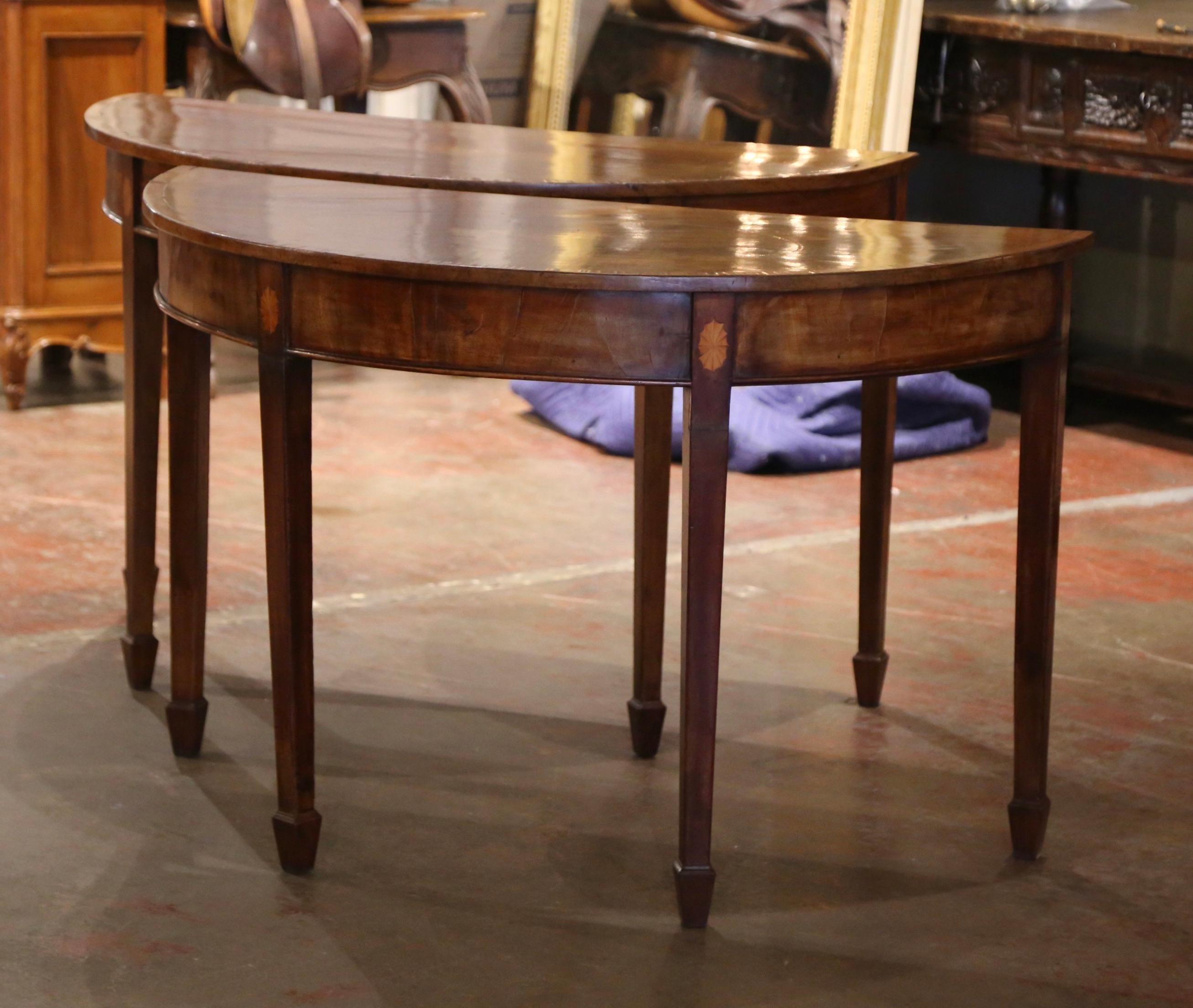 Decorate an entryway with this elegant pair of antique consoles. Crafted in England, circa 1870 and shaped as half moon, each Sheraton style table stands on four tapered legs, each accented with intricate inlaid detailing and ending in square spade