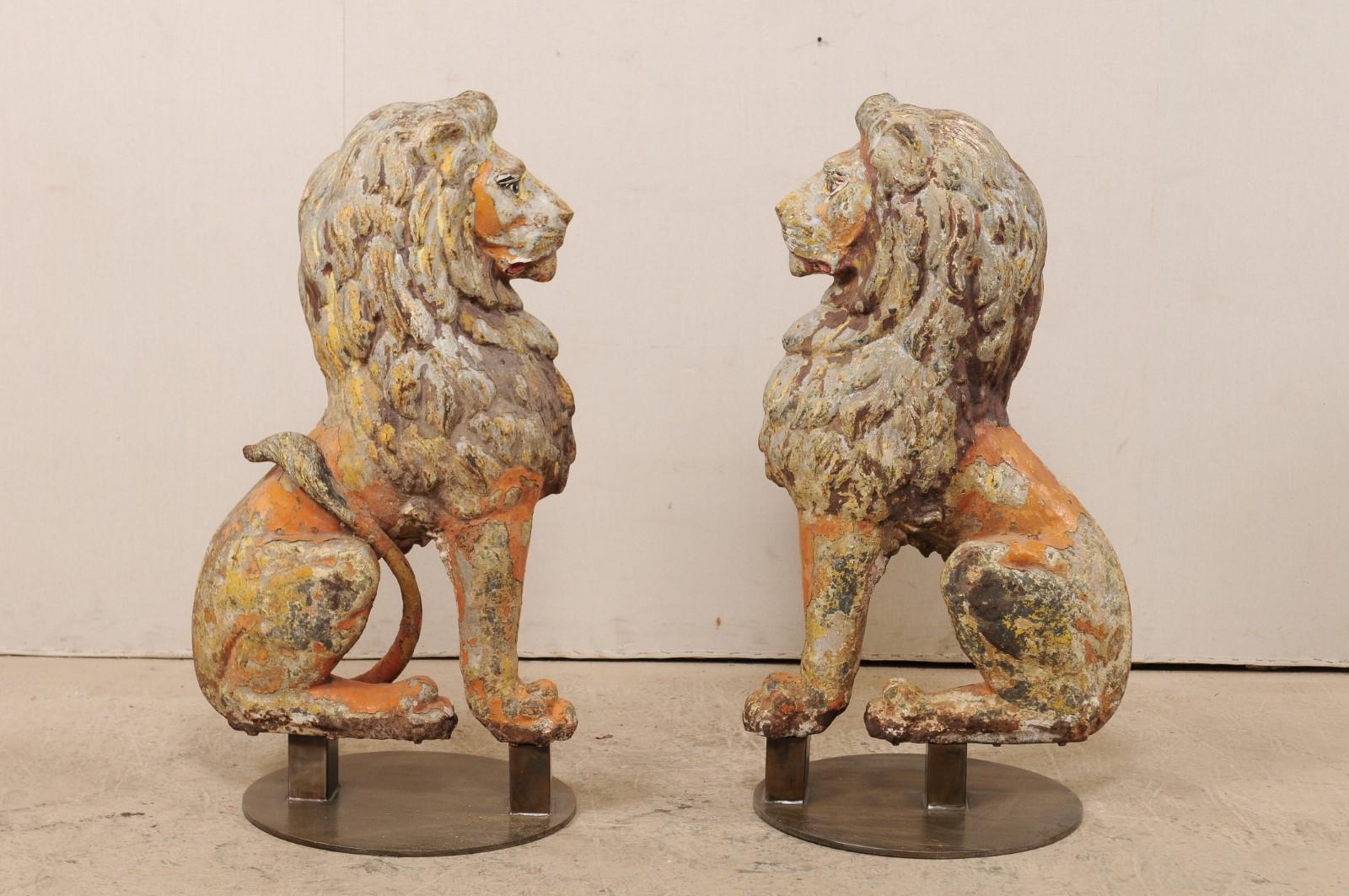 A pair of English sitting lions of cast-iron from the 19th century on stands. This antique pair of cast-iron lions from England are each one half of a pair, with front position being shown at side to create a perfectly seated pair, which have then