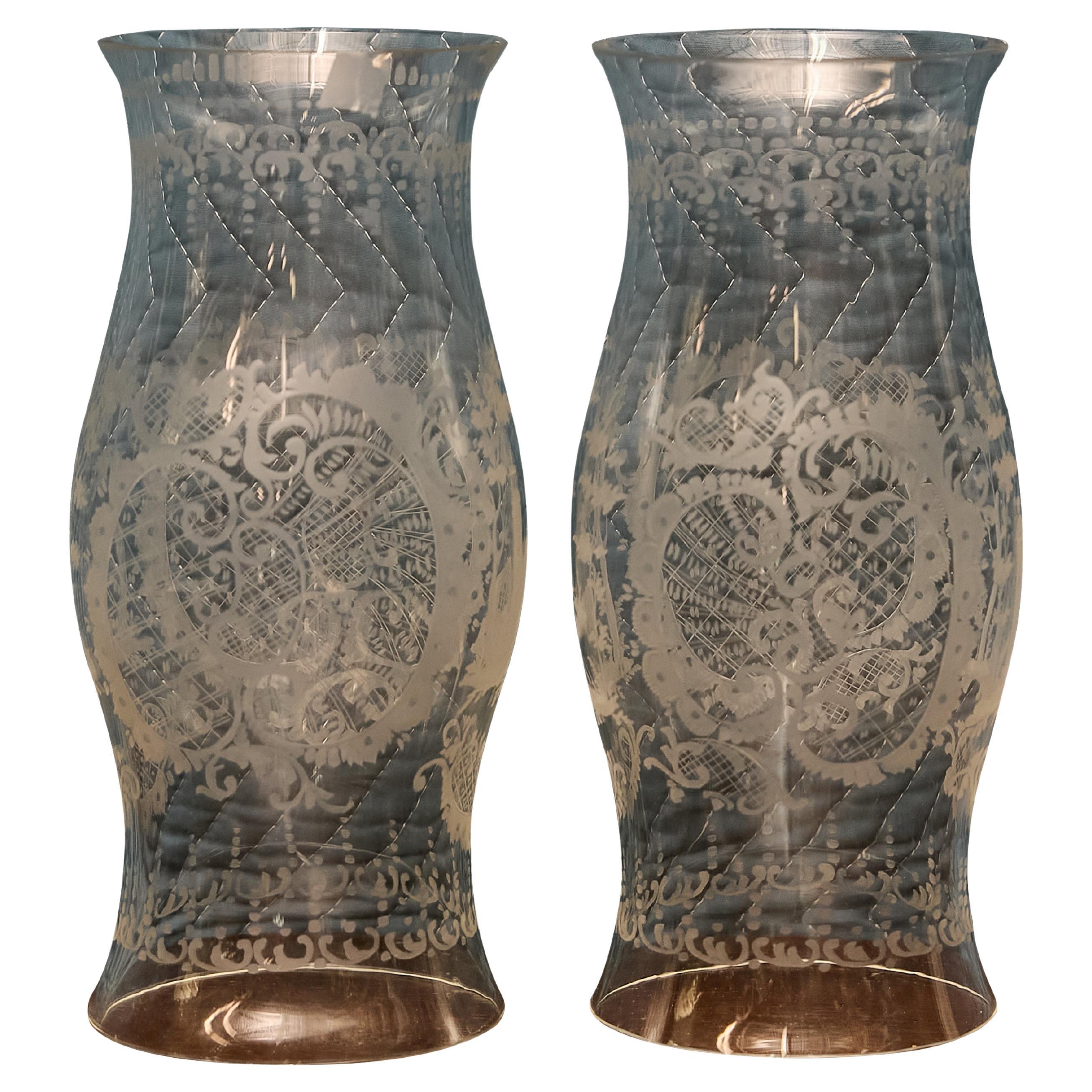 Questa coppia di uragani in vetro inglese del XIX secolo presenta una decorazione delicatamente incisa con medaglioni foliati simmetrici, cartigli e bordi a volute. Ogni paralume presenta una silhouette a clessidra rovesciata che si svasa