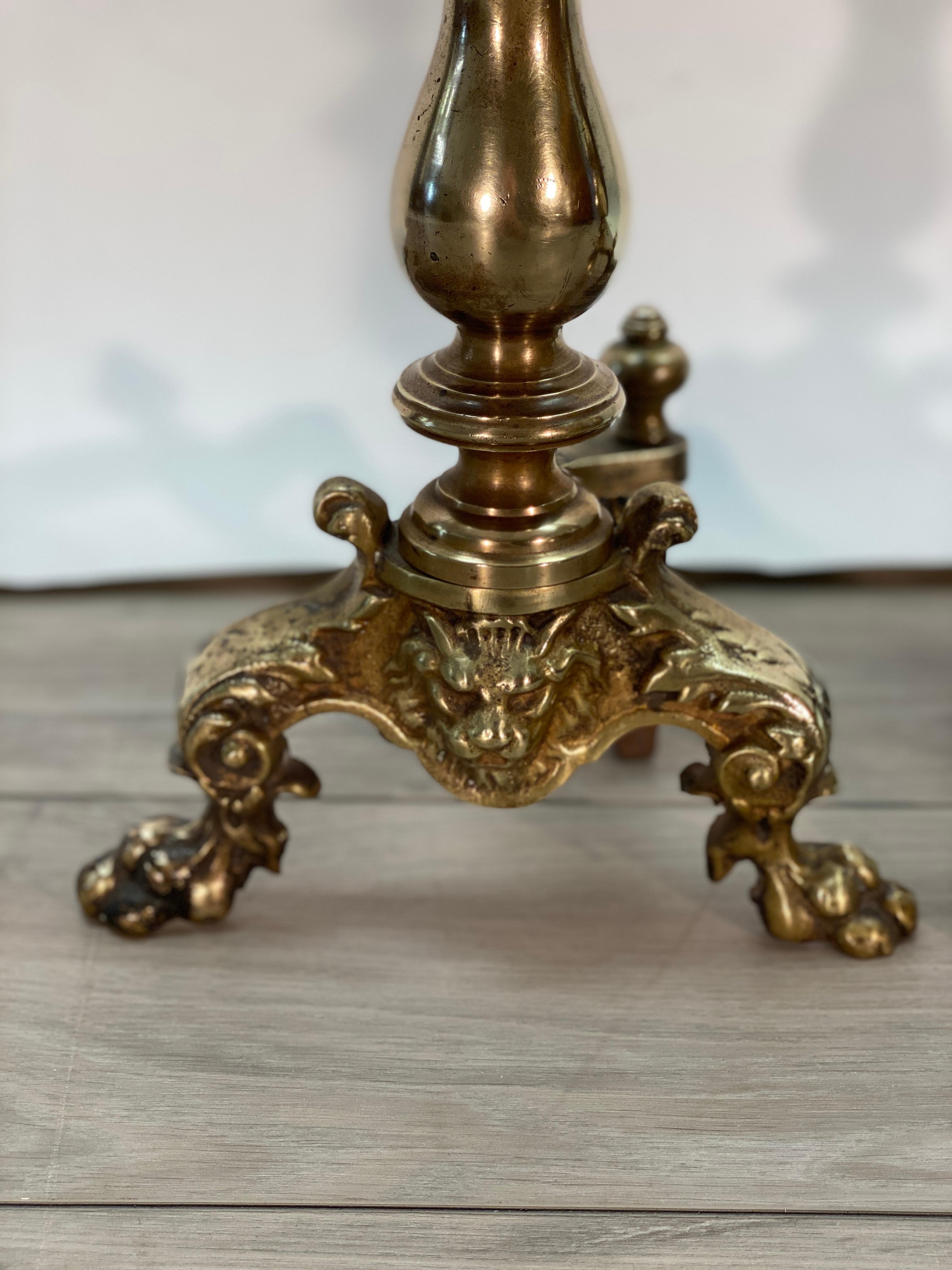 English brass andirons, Both resting on paw feet adorned with a central Lions face. The center rises with turned brass urn form terminating into spires. Very handsome and warm patina.