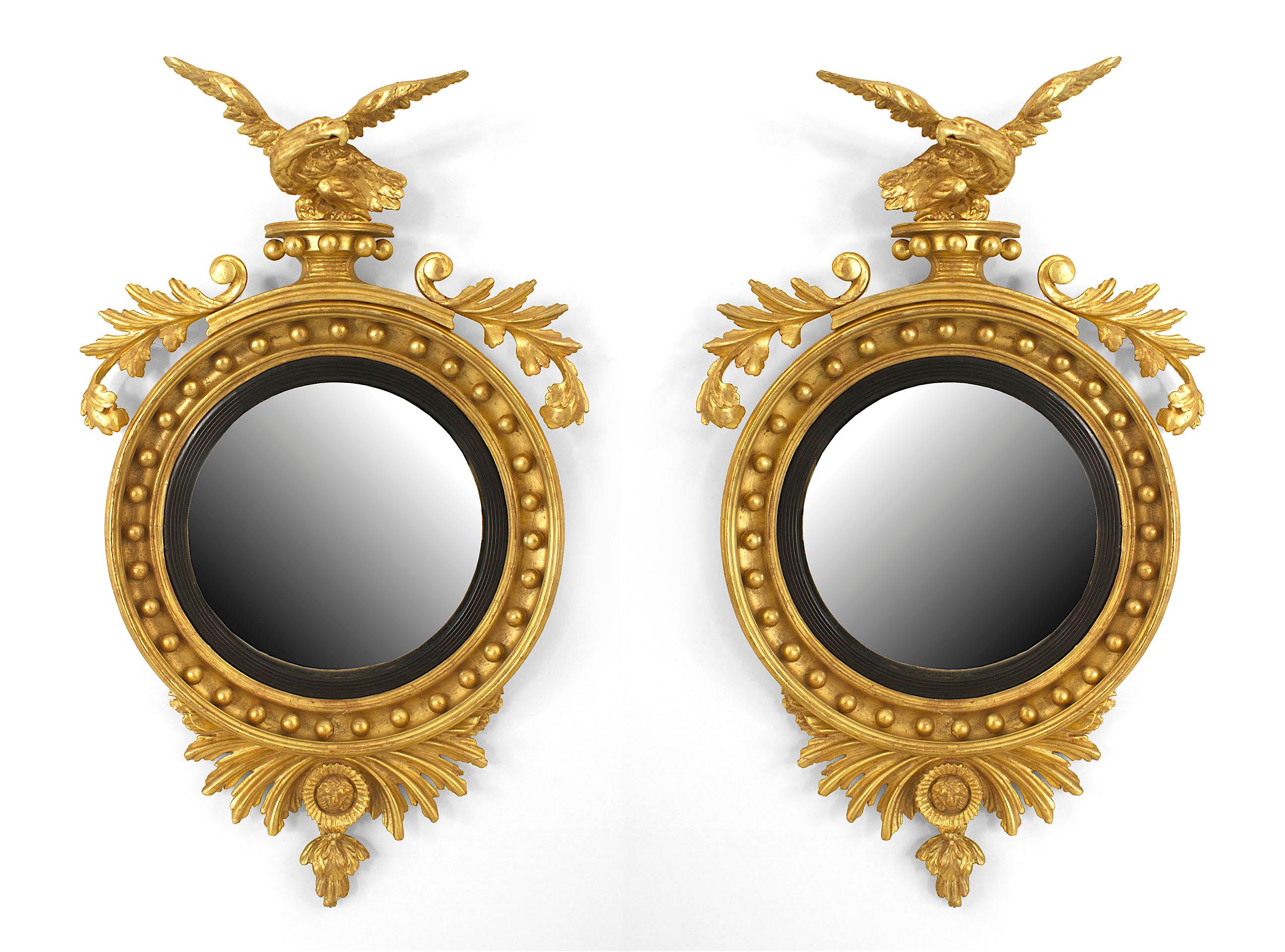 Pair of English Georgian first quarter of 19th century gilt round convex wall mirror with carved scroll and leaf design with an eagle top and finial bottom.