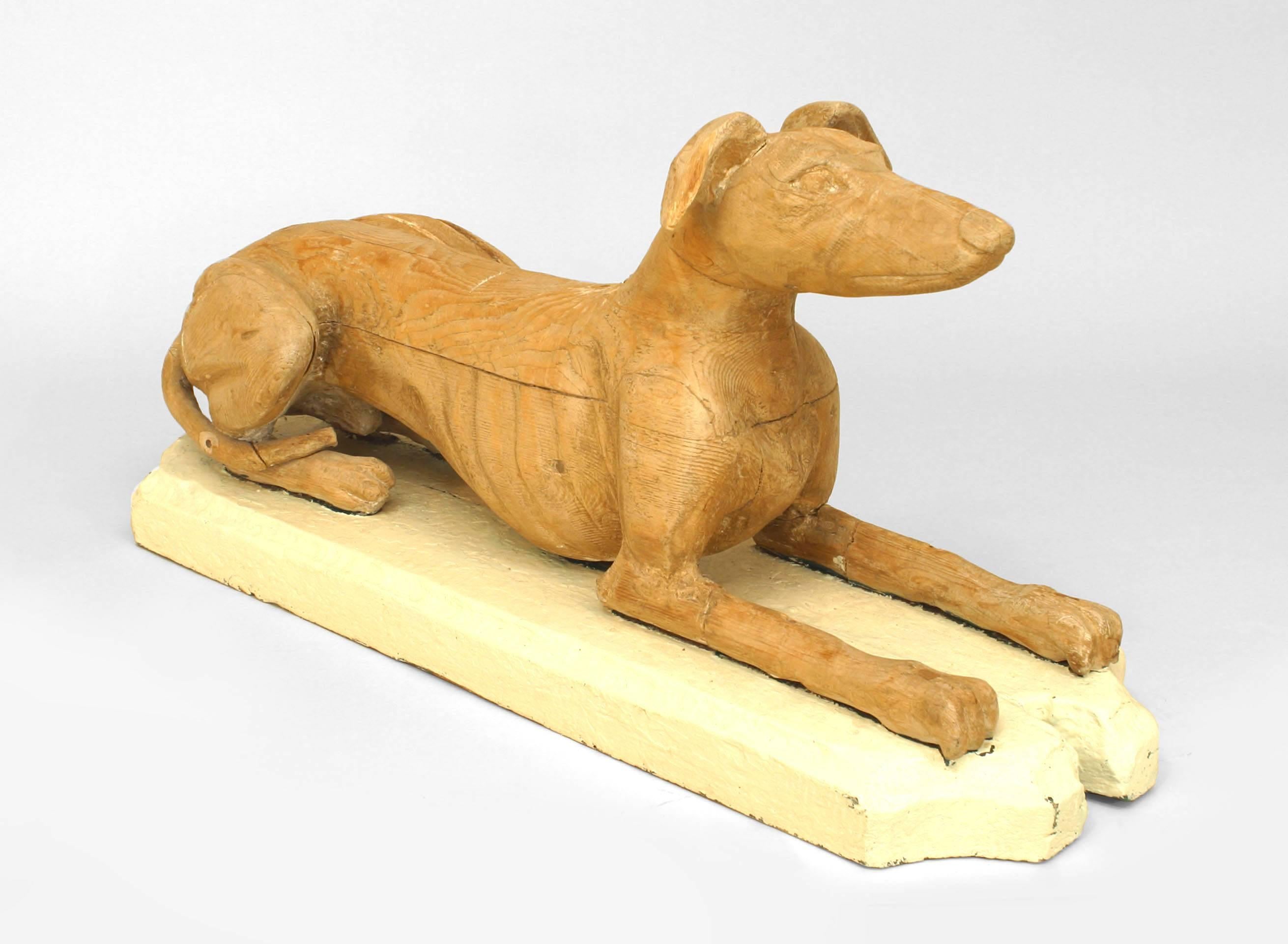 Pair of 19th century English sculptures of life-sized reclining dogs composed of stripped wood and resting upon painted wooden bases.